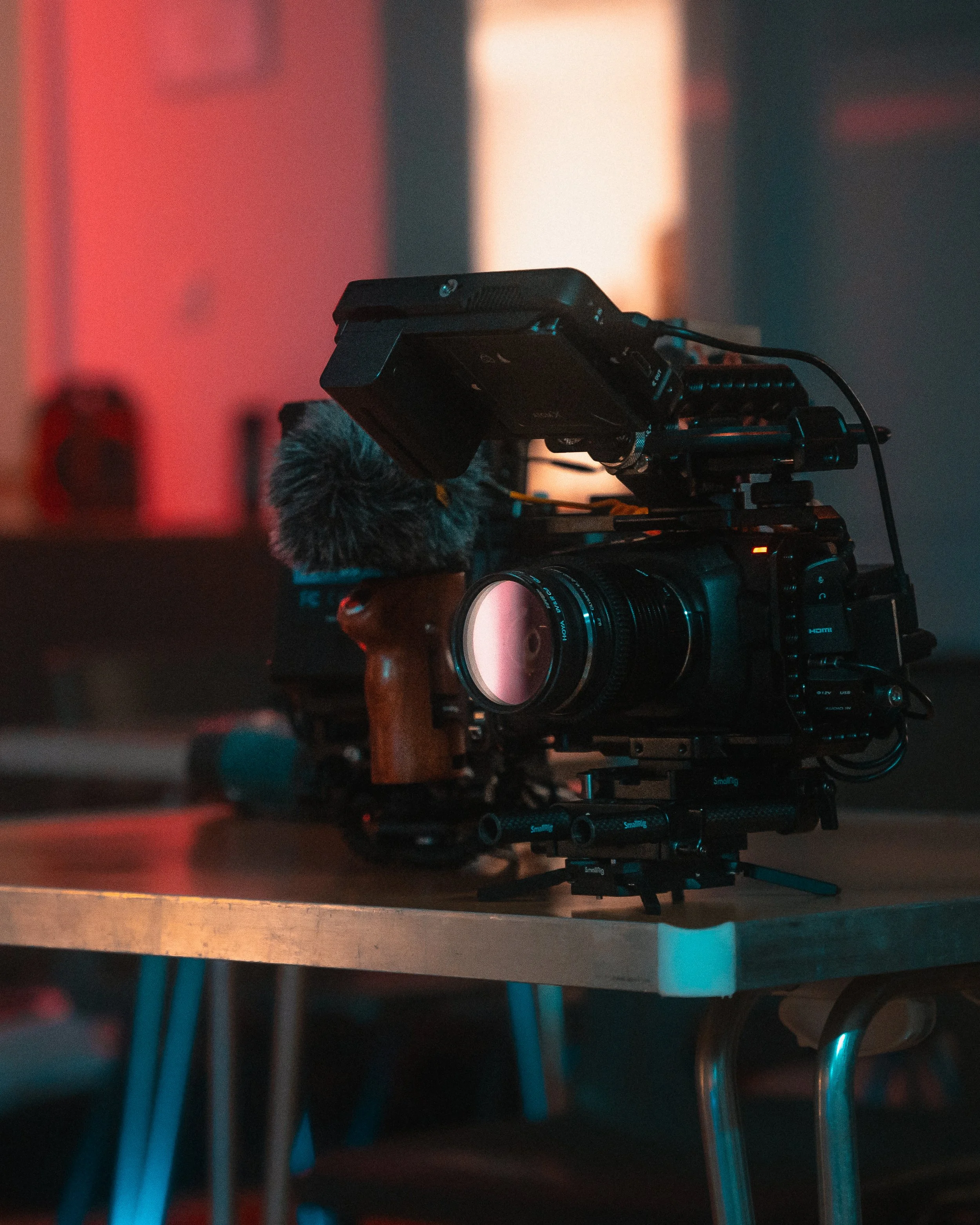 Camera rig with a microphone and monitor set up on a wooden table in a dimly lit room with colorful lighting.