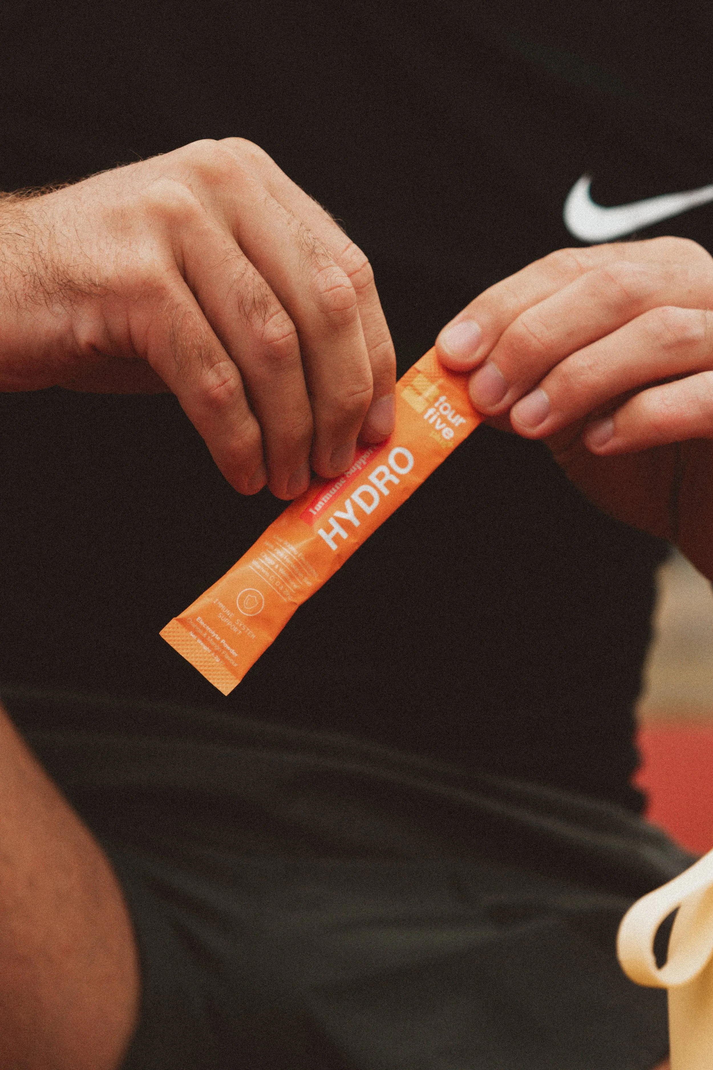 Person holding an orange packet labeled 'HYDRO' with a Nike logo visible on their shirt.