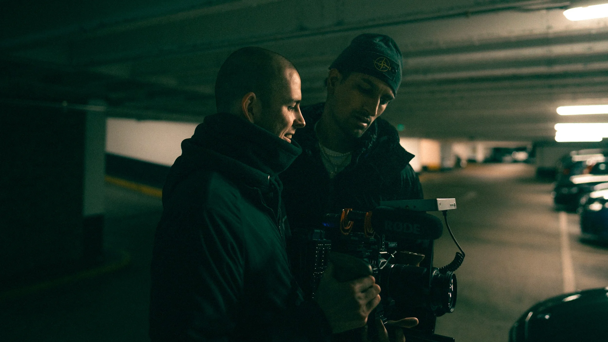 Two men in a parking garage operating a professional video camera together.
