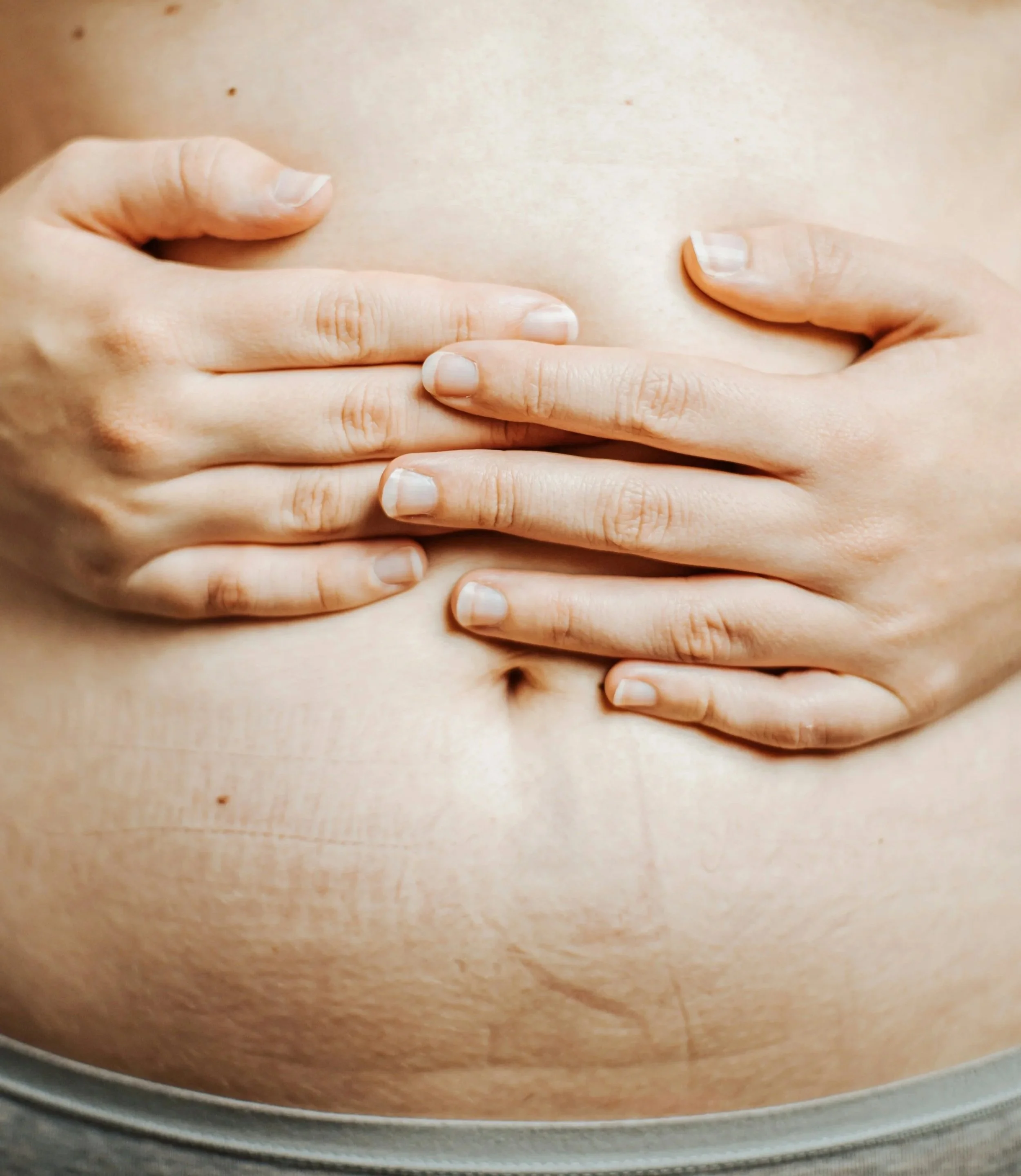 Close-up of a person's abdomen with hands covering the area.