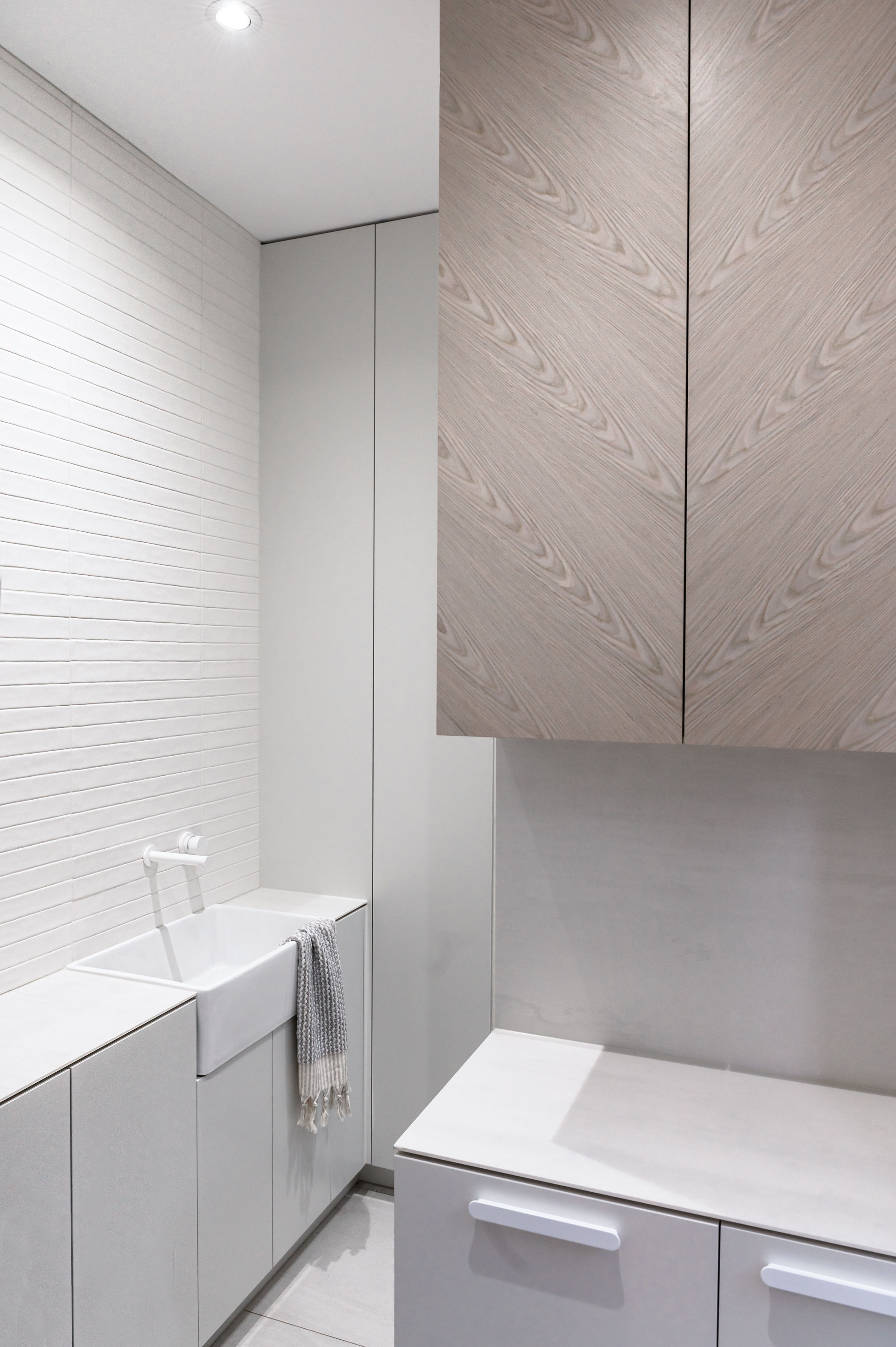 Modern laundry room with white brick wall, a white utility sink, light gray cabinets, and wooden upper cabinets with a chevron pattern.