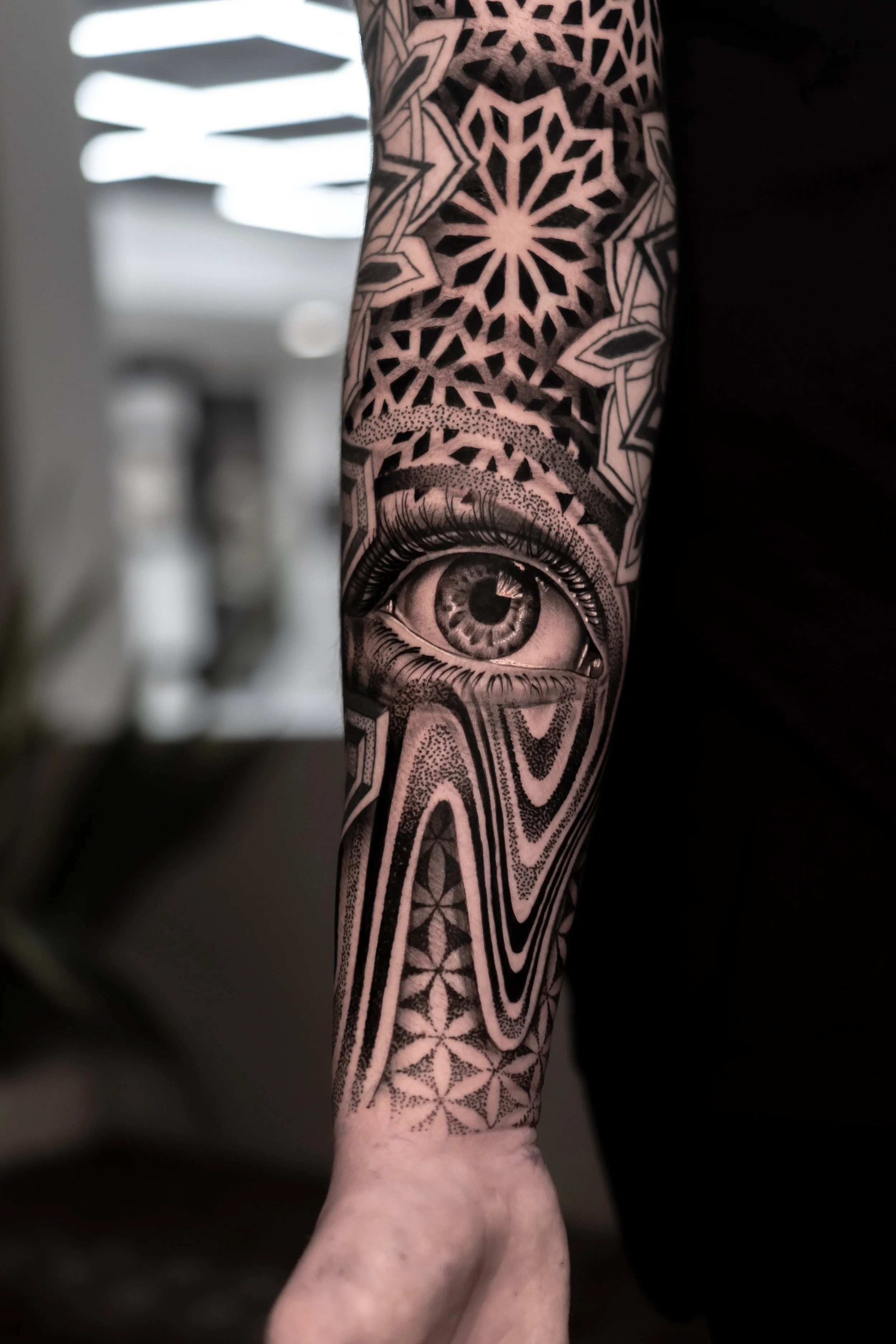 Tattooed arm featuring an eye, geometric patterns, and star shapes in black ink.