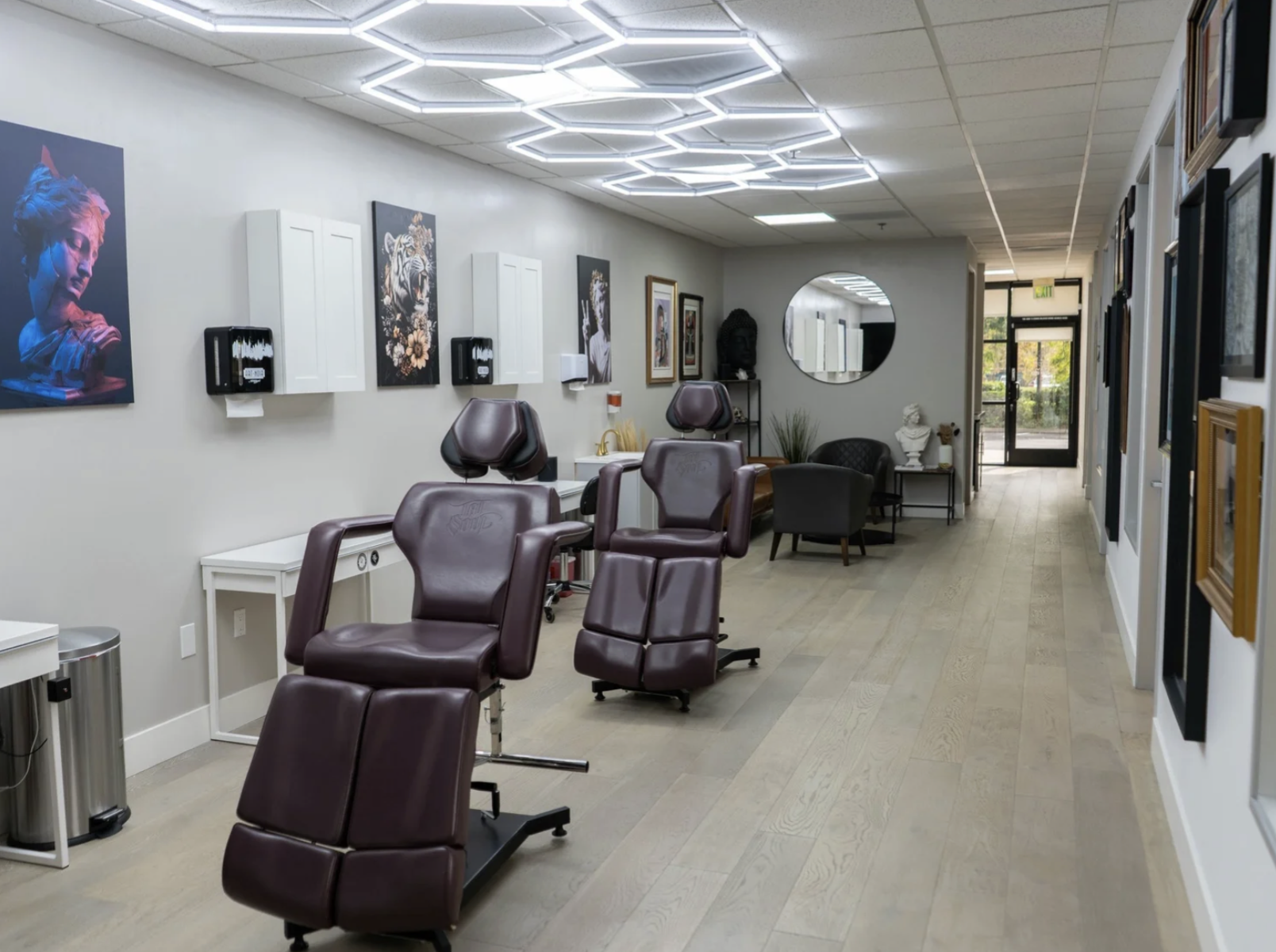 Interior of a tattoo parlor with multiple tattoo chairs, artwork on the walls, and a seating area near the back