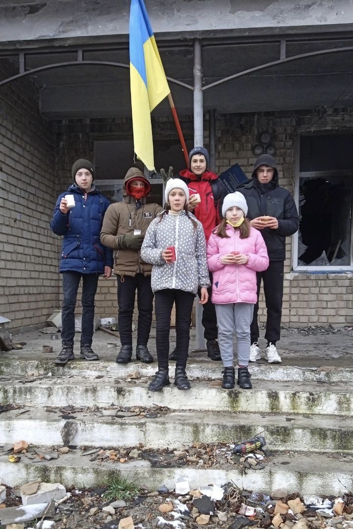  Students warm themselves with candles in front of their bombed school. 
