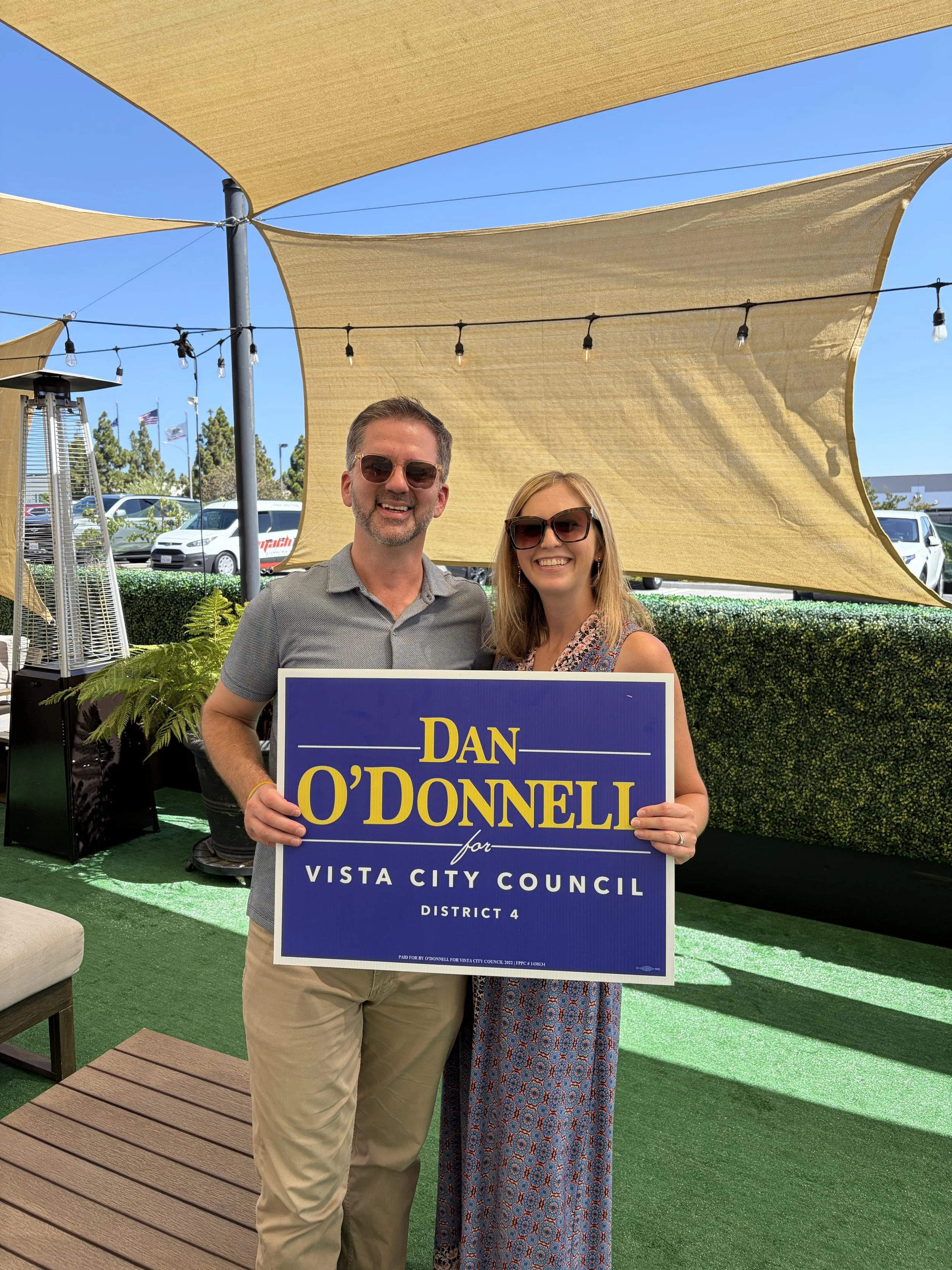 Deputy Mayor and Vista City Councilmember Dan O'Donnell with his wife Allie holding up his re-election sign from his campaign kick-off and Burtech Family Vineyard in Vista, CA business district