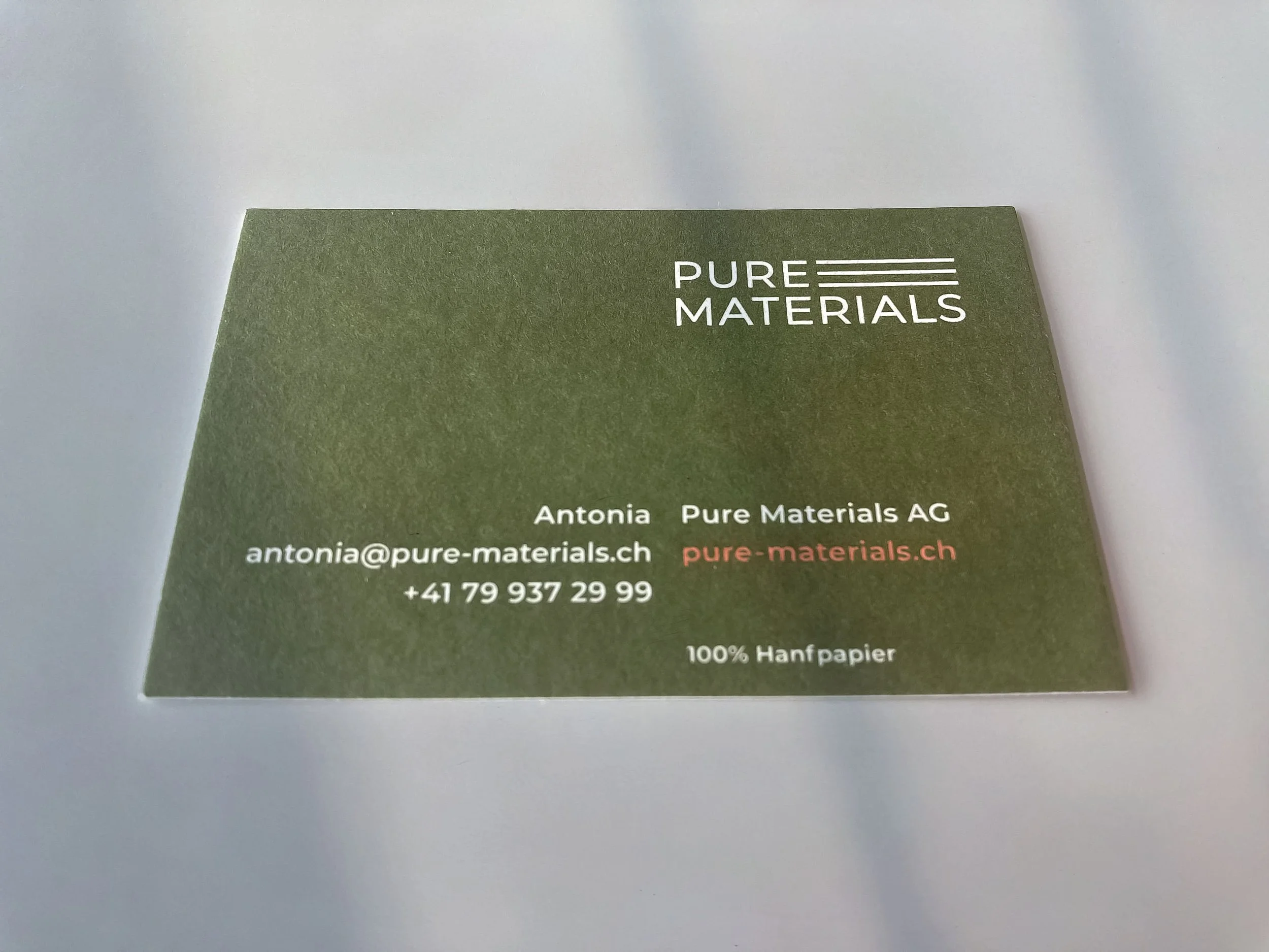 Grüne Visitenkarte aus Hanfpapier mit Pure Materials Logo und Kontaktangaben