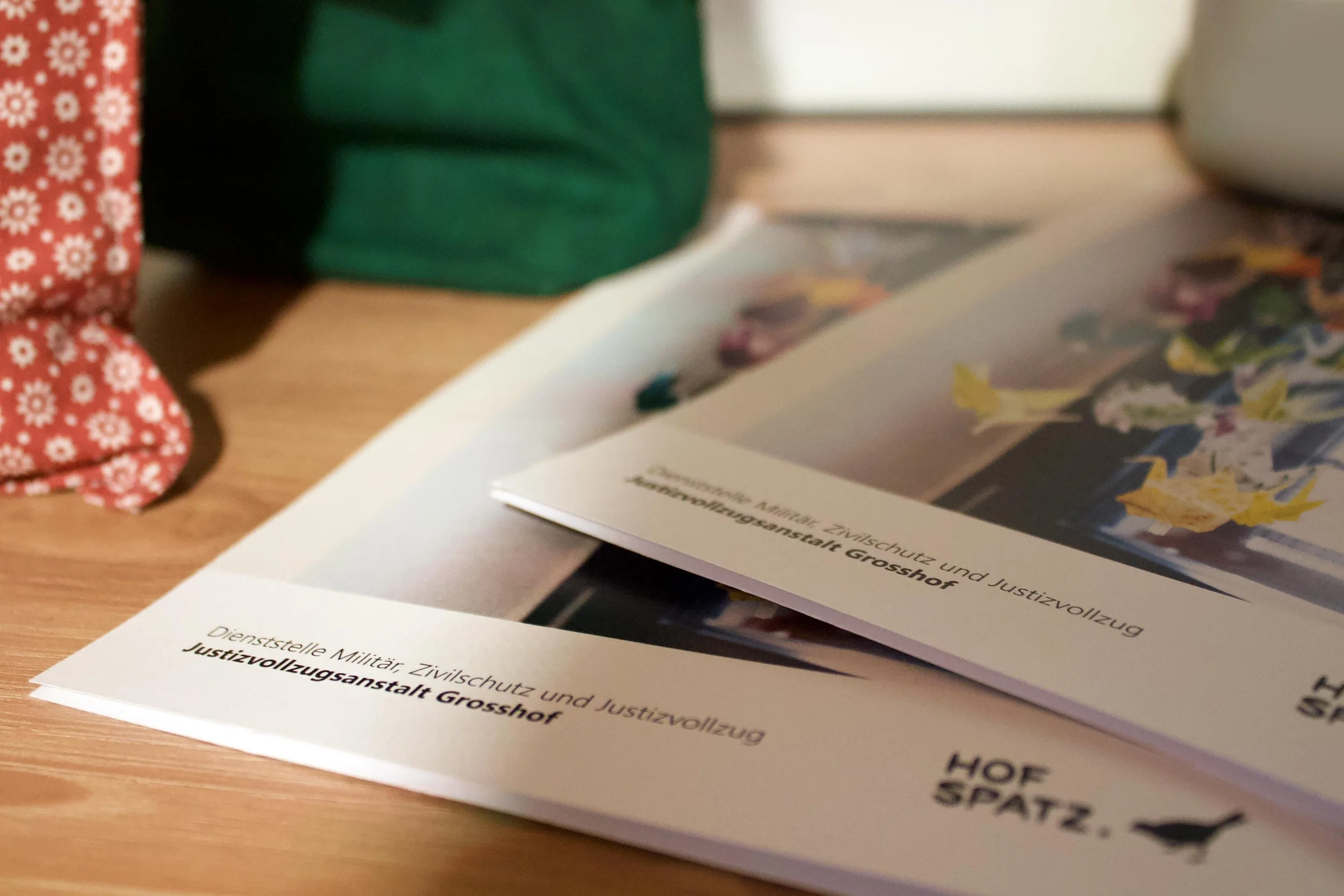 Printprodukte der JVA Grosshof mit Hofspatz-Branding auf einem Holztisch.