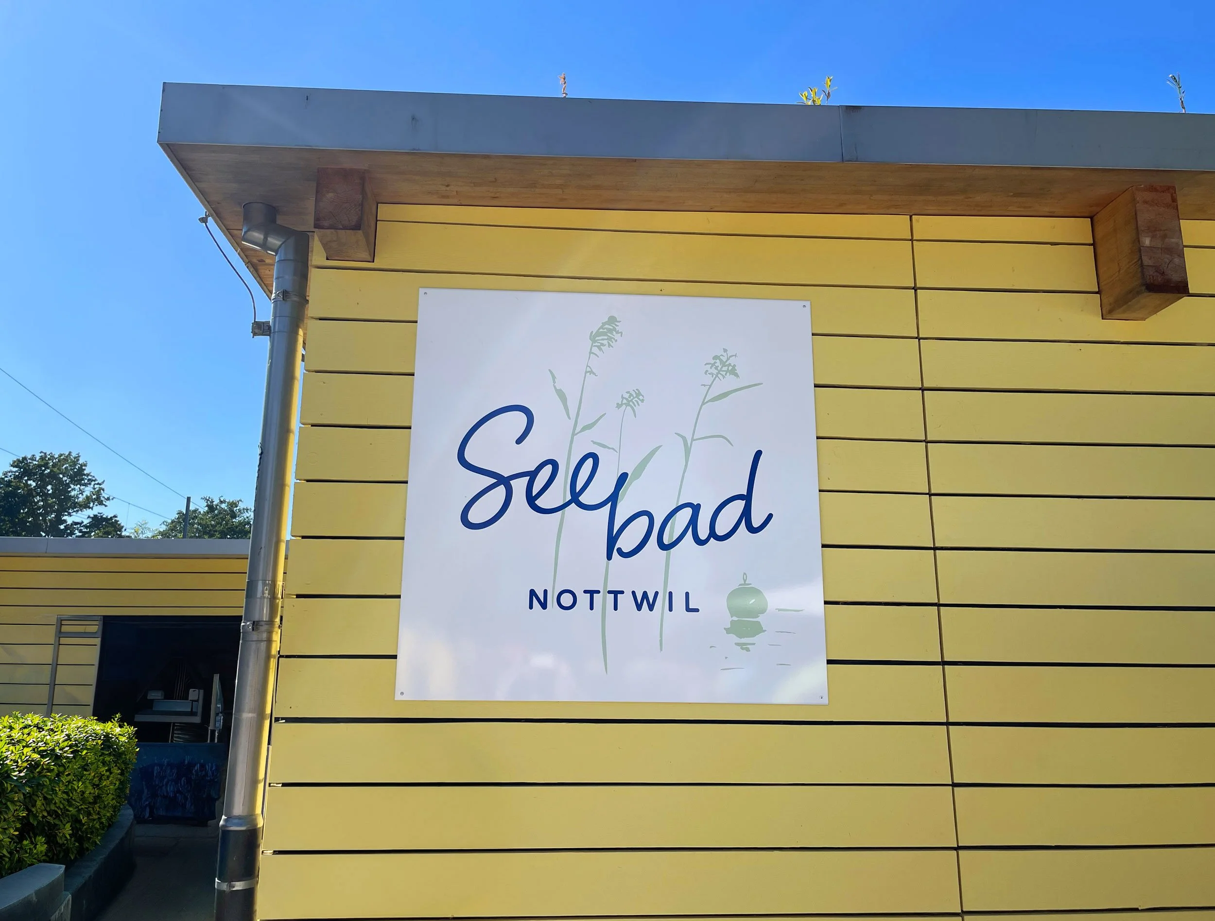 Seebad-Nottwil-Logotafel an der gelben Holzfassade des Badi-Gebäudes
