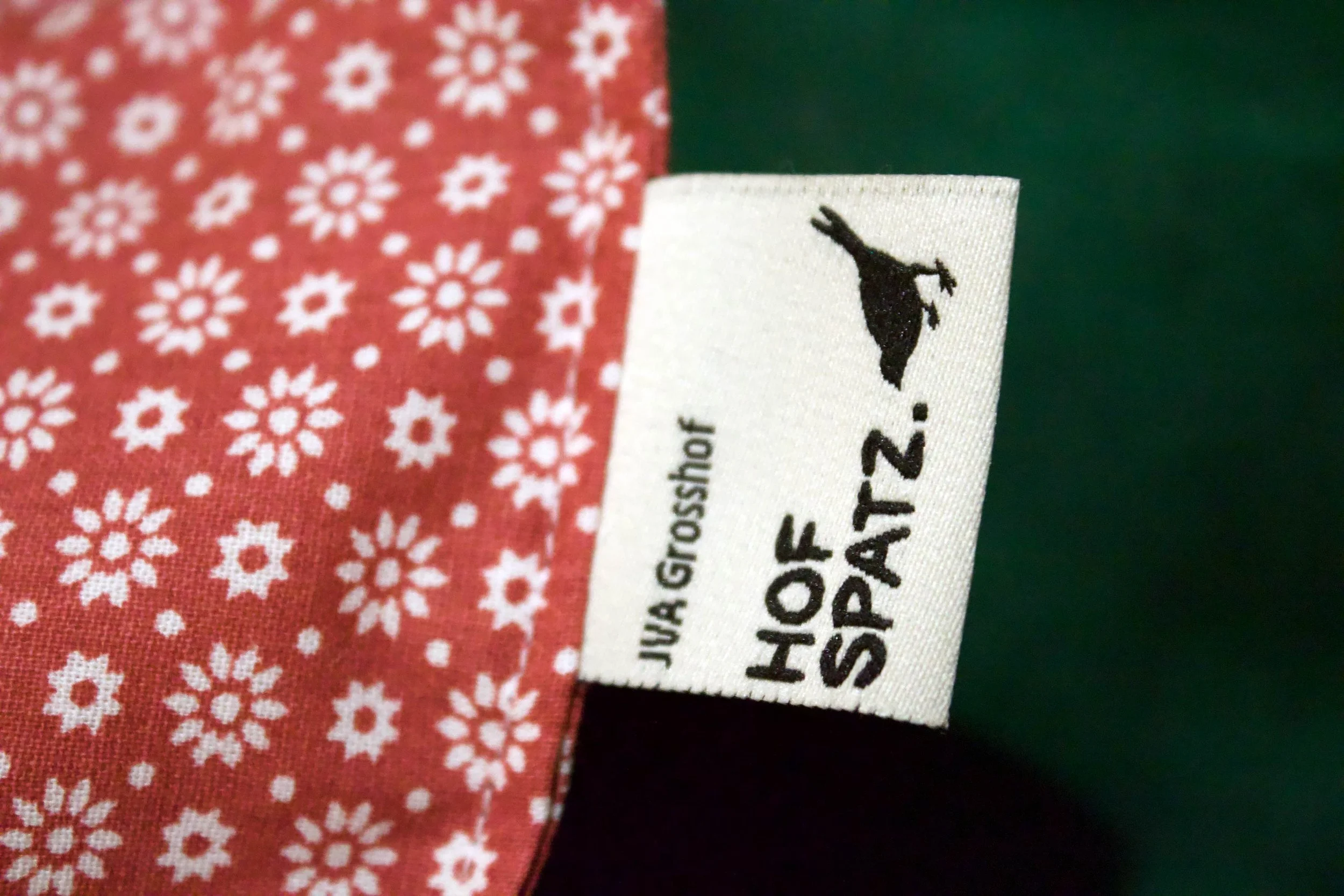 Nahaufnahme eines Hofspatz-Labels an einem roten Stoffbeutel mit Blumenmuster.