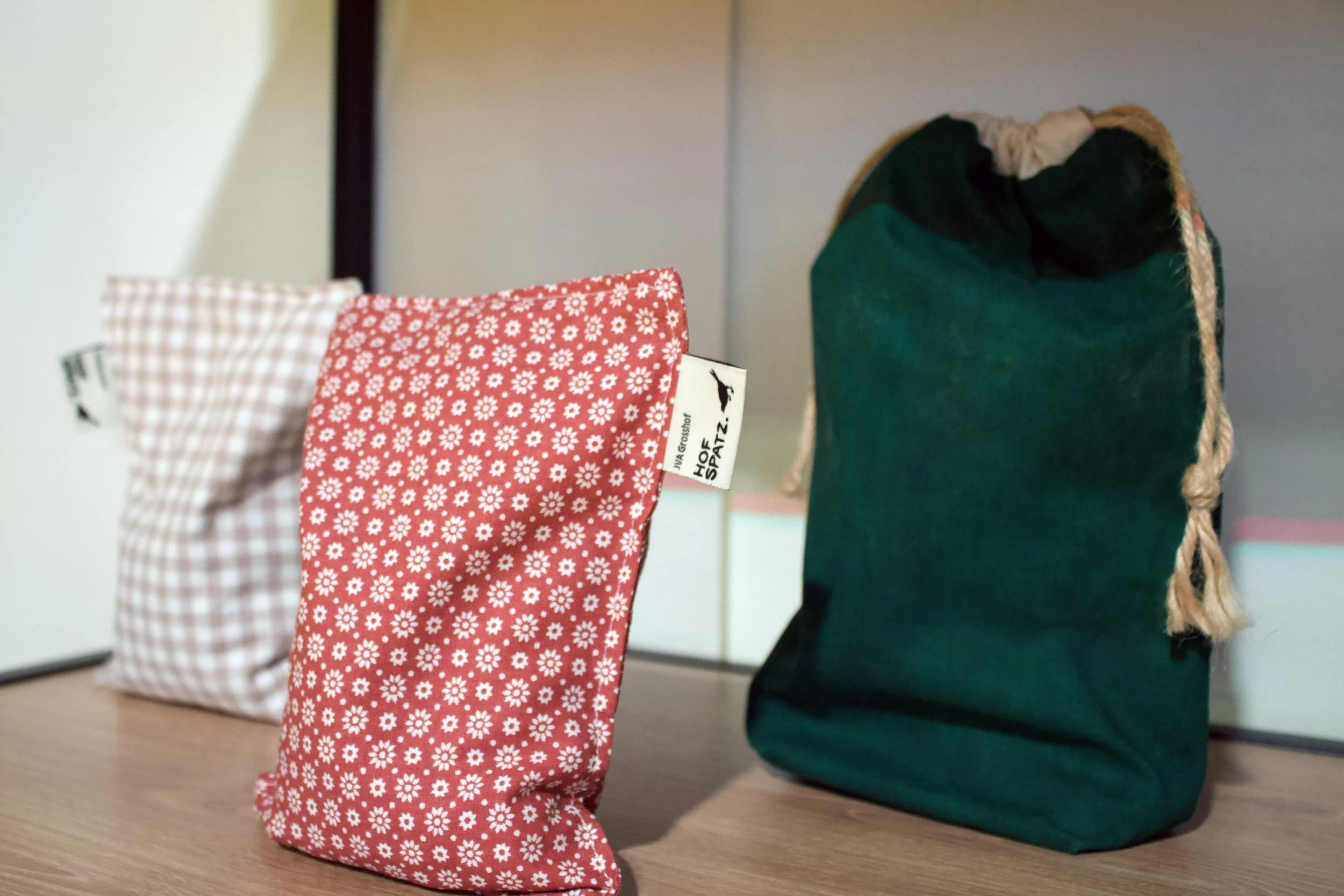 Drei genähte Hofspatz-Stoffsäckli in unterschiedlichen Stoffen mit sichtbarem Label der JVA Grosshof.