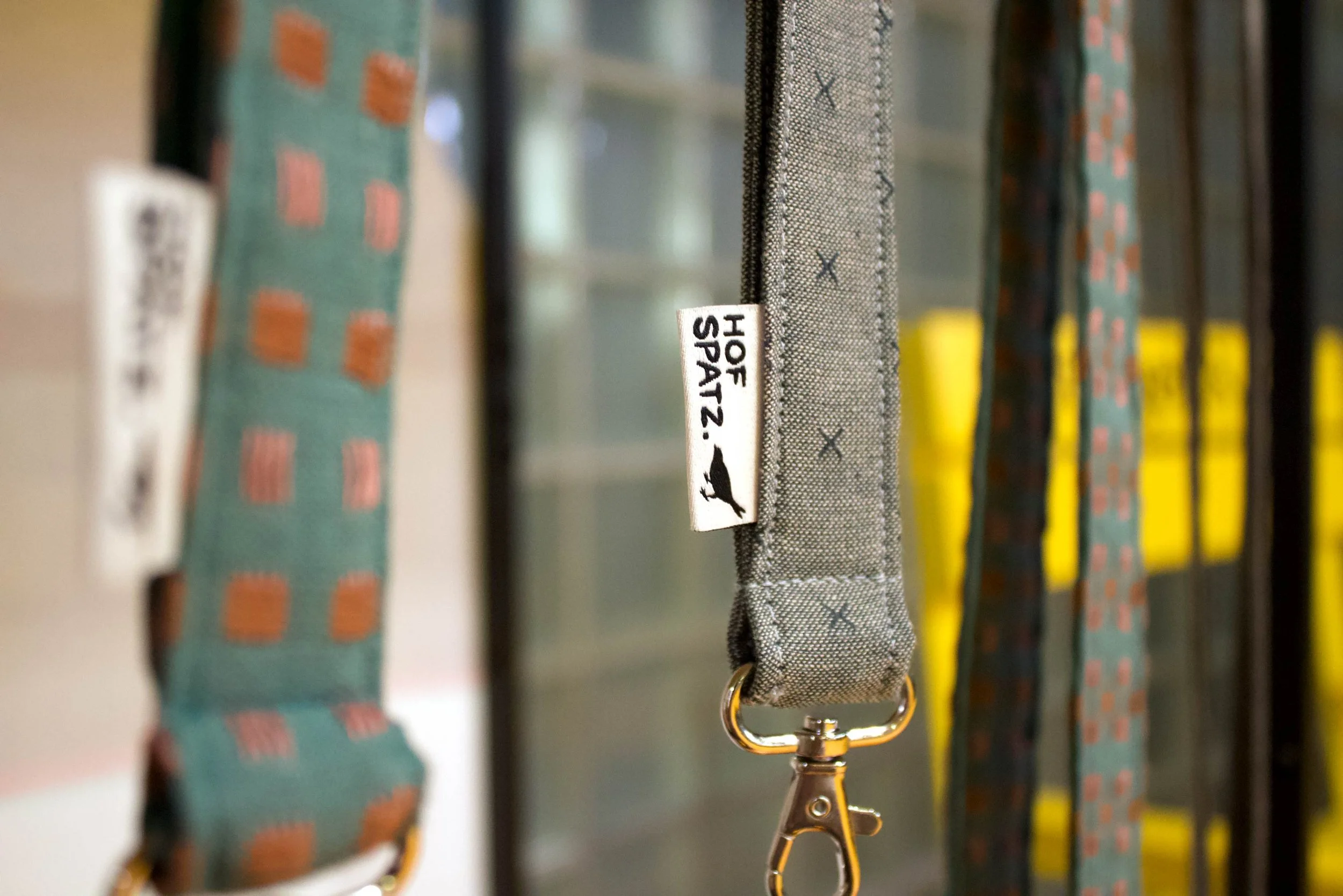 Detailaufnahme eines grauen Schlüsselbands mit Metallkarabiner und Hofspatz-Label.