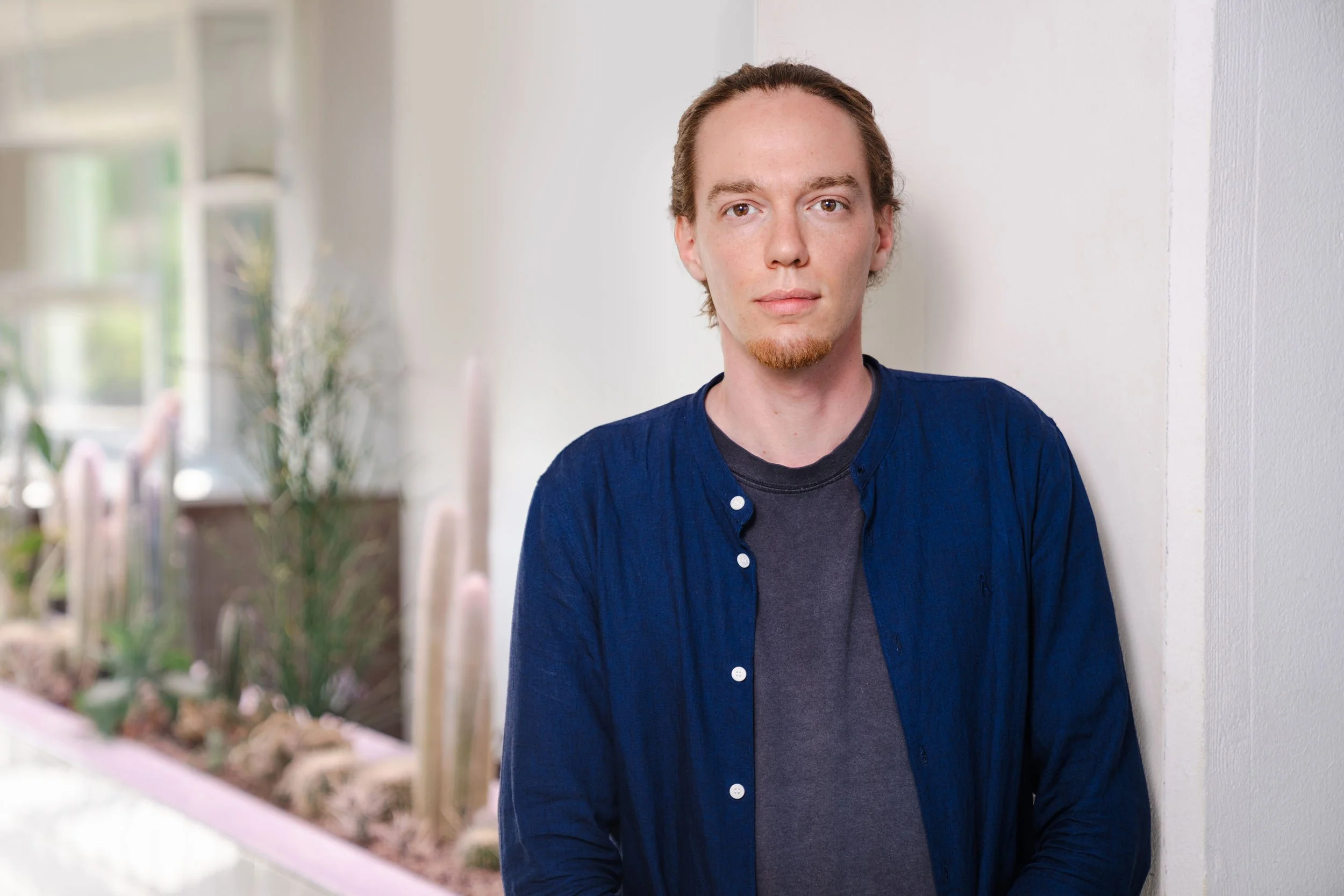 Eine freundlicher Mann mit rötlichen Haaren steht in einem lichtdurchfluteten Raum mit Kakteen im Hintergrund.