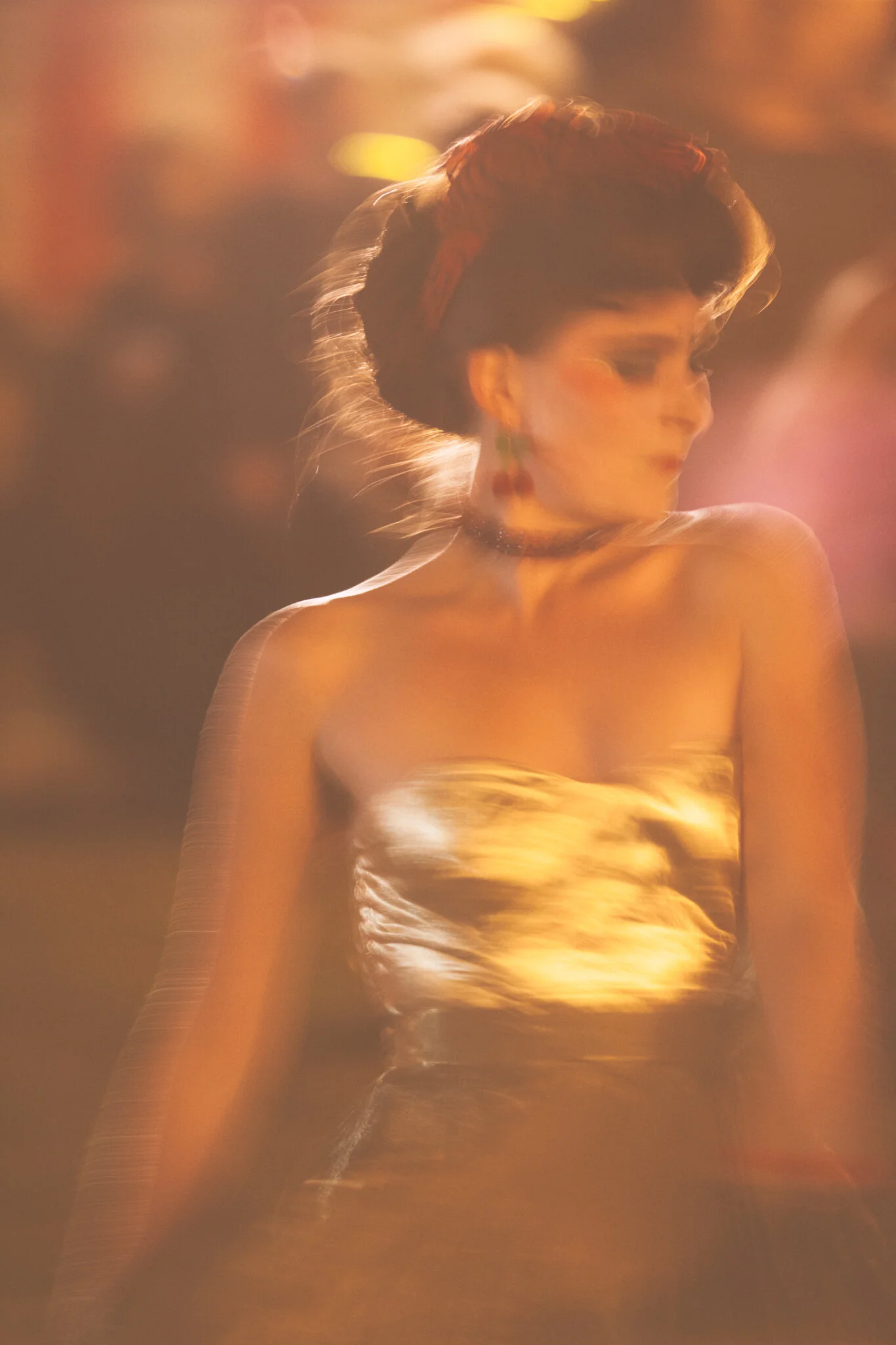 Farbiger, unscharfer Porträt eines Models bei Nacht mit leuchtendem, goldenem Kleid und rotem Lippen, mit blurry Lichter im Hintergrund.