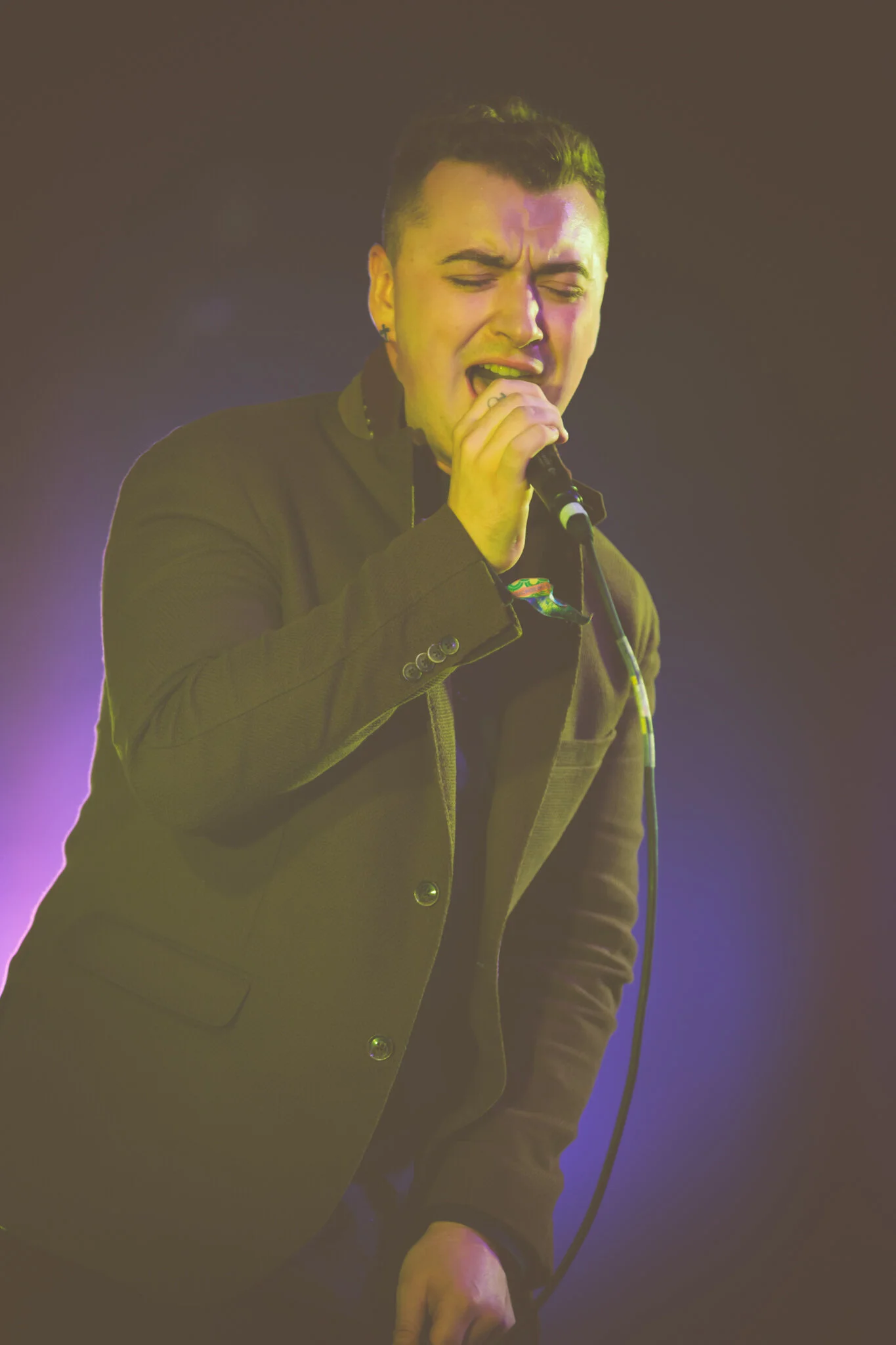 Ein junger Sam Smith singt leidenschaftlich in ein Mikrofon auf einer Bühne, mit einem intensiven Ausdruck im Gesicht.