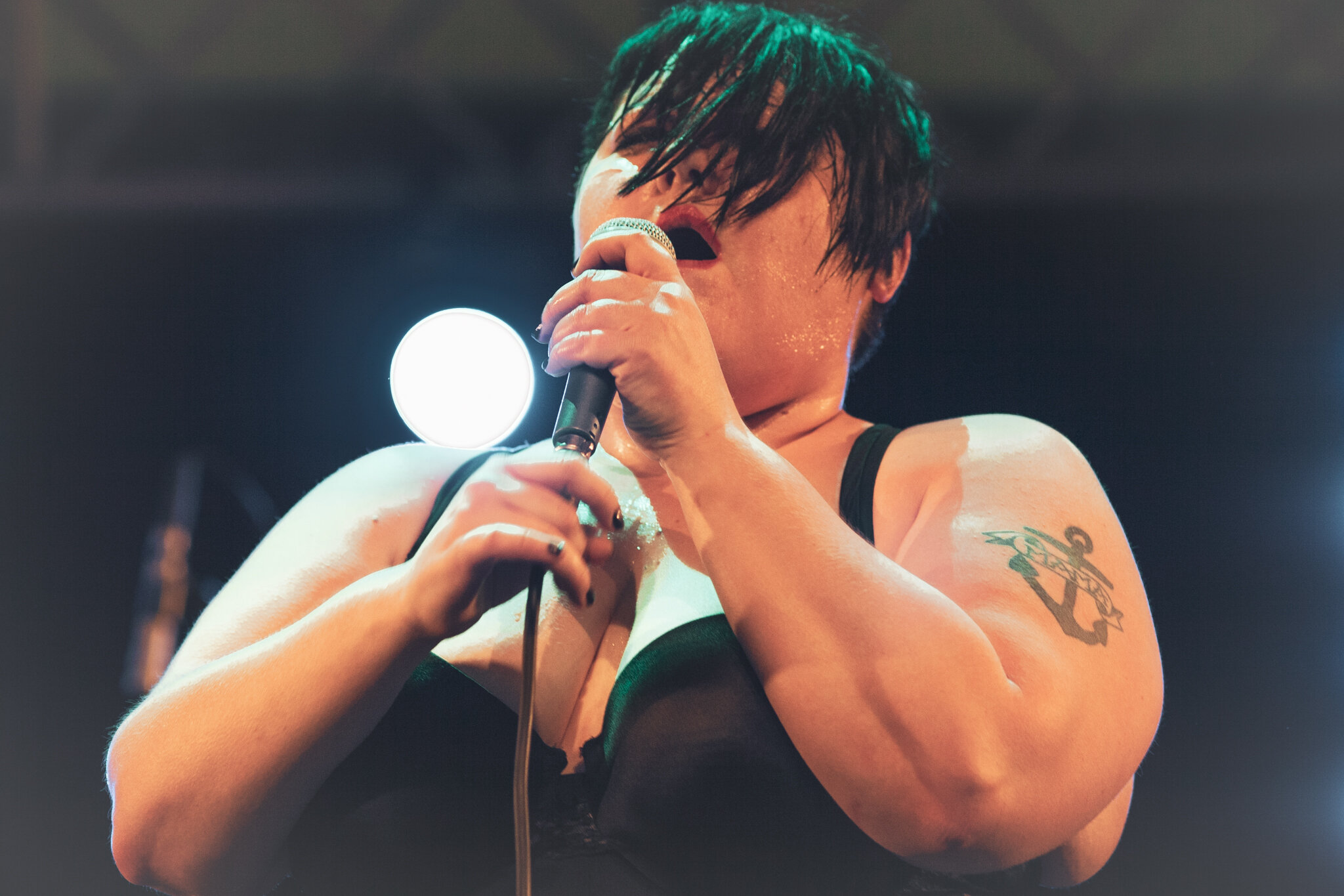 Beth Ditto mit nassen schwarzen Haaren, die in schwarzem Oberteil singt, während sie eine Mikrofon hält, auf einer Bühne bei einem Live-Auftritt.