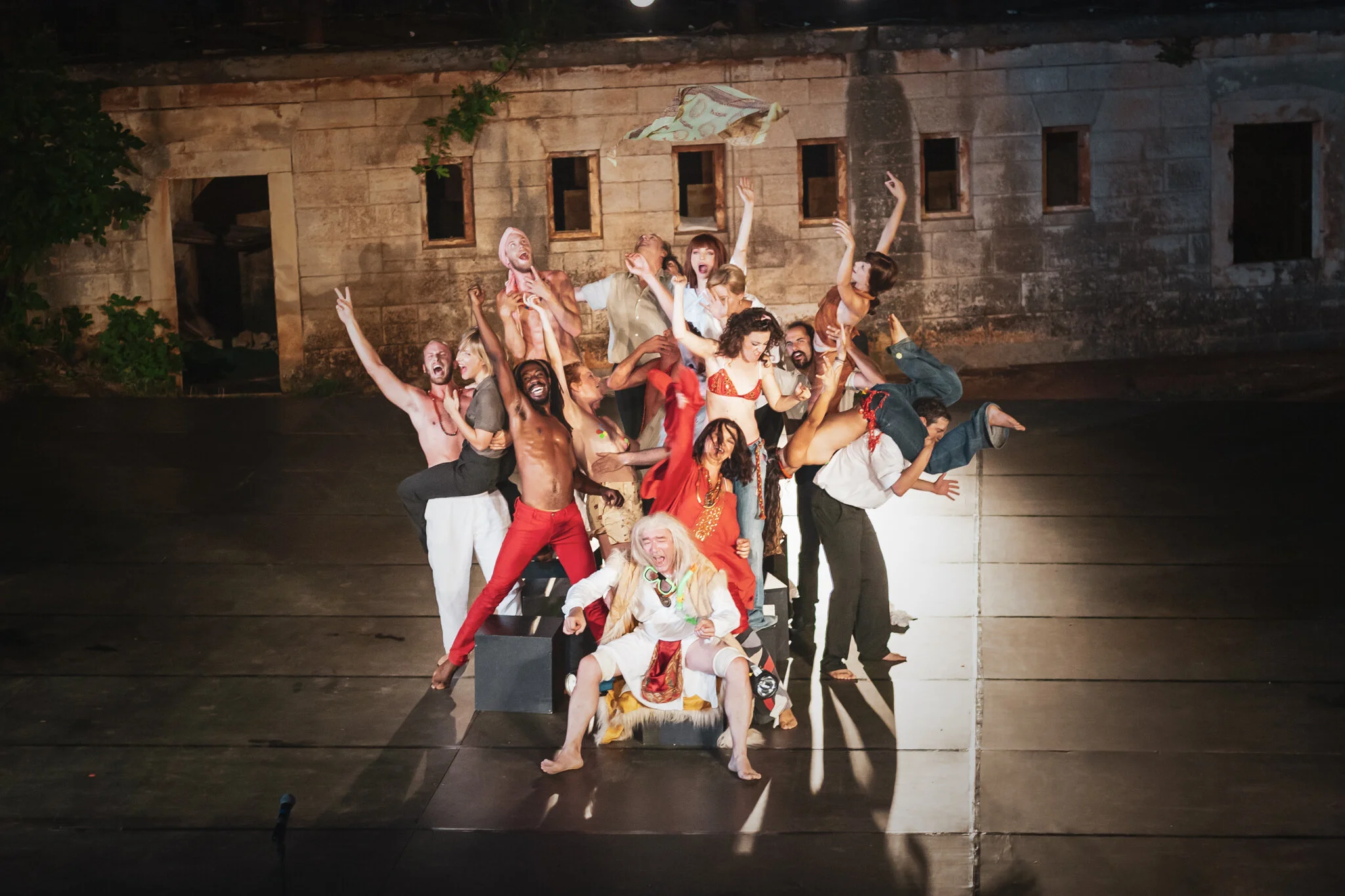 Theatergruppe auf der Bühne, teilt einen humorvollen Moment, im Hintergrund eine alte Steinwand