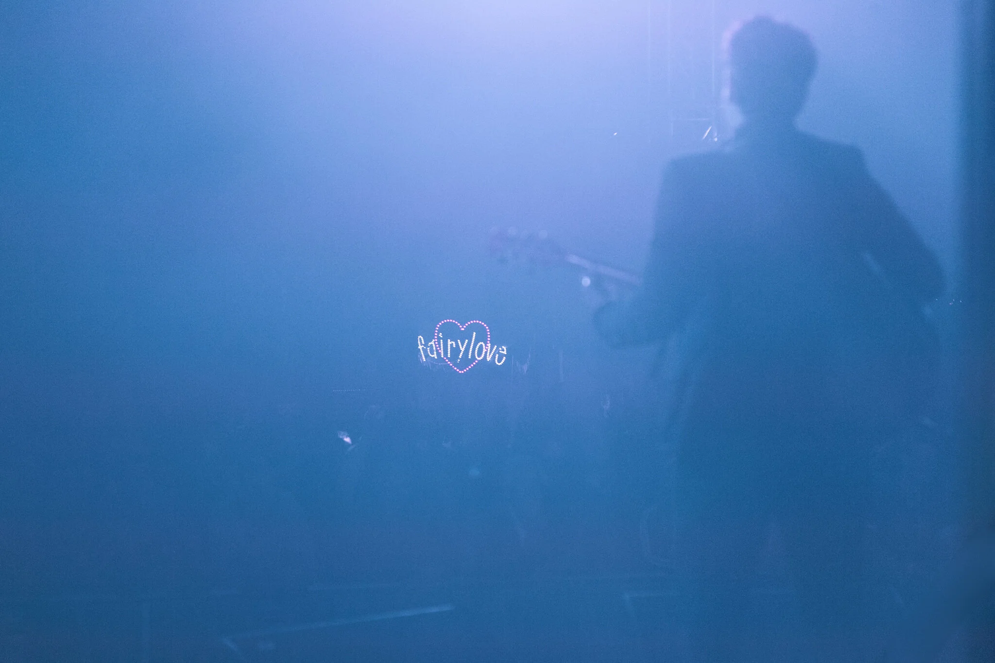 Reflexion eines Mannes in einer blauen Wand mit einem kleinen leuchtenden Herz und Text 'fairy love'