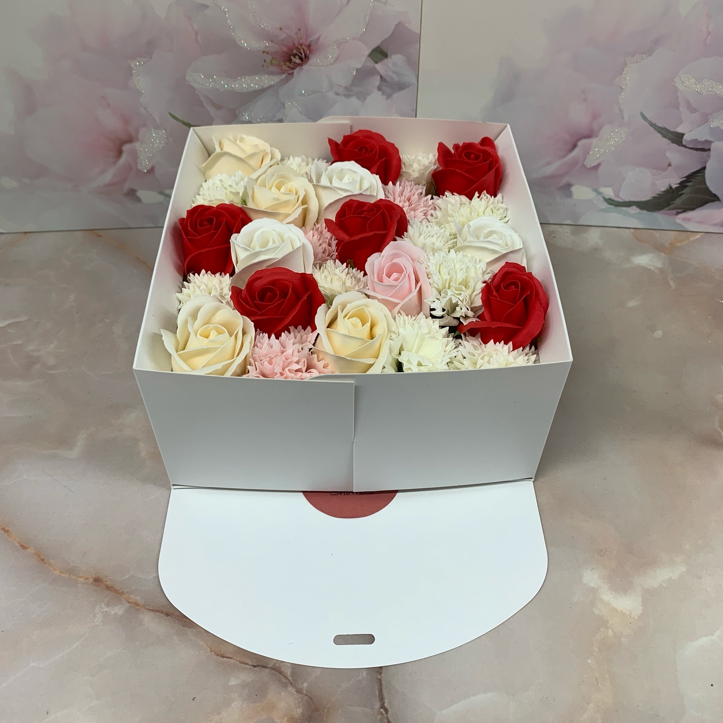 a white ribboned square gift box containg a mix of white red and cream scented soap roses and carnations