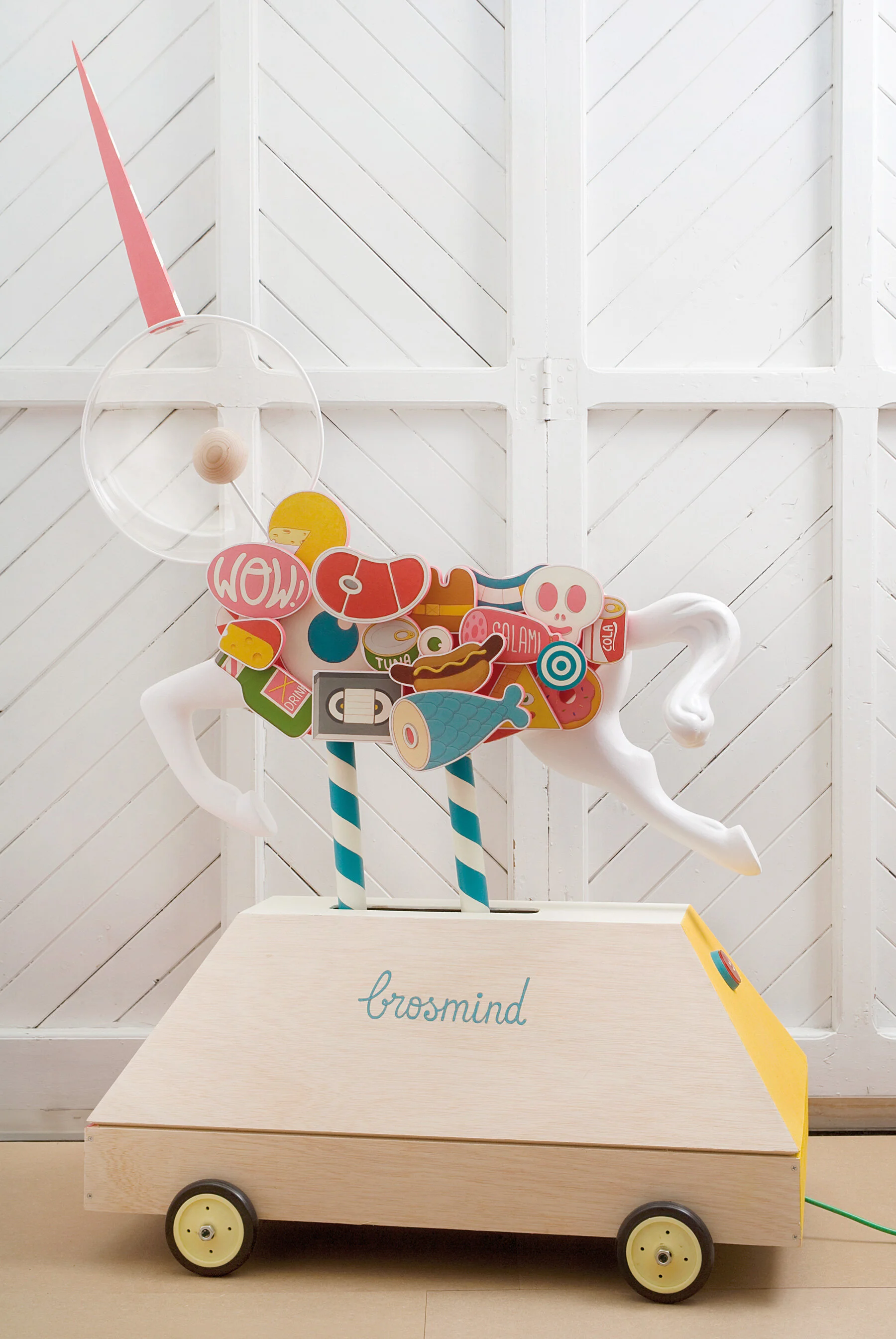 Mechanical unicorn ride sculpture with cutout wooden food figures like hot dogs, fish, and cheese by Brosmind. 