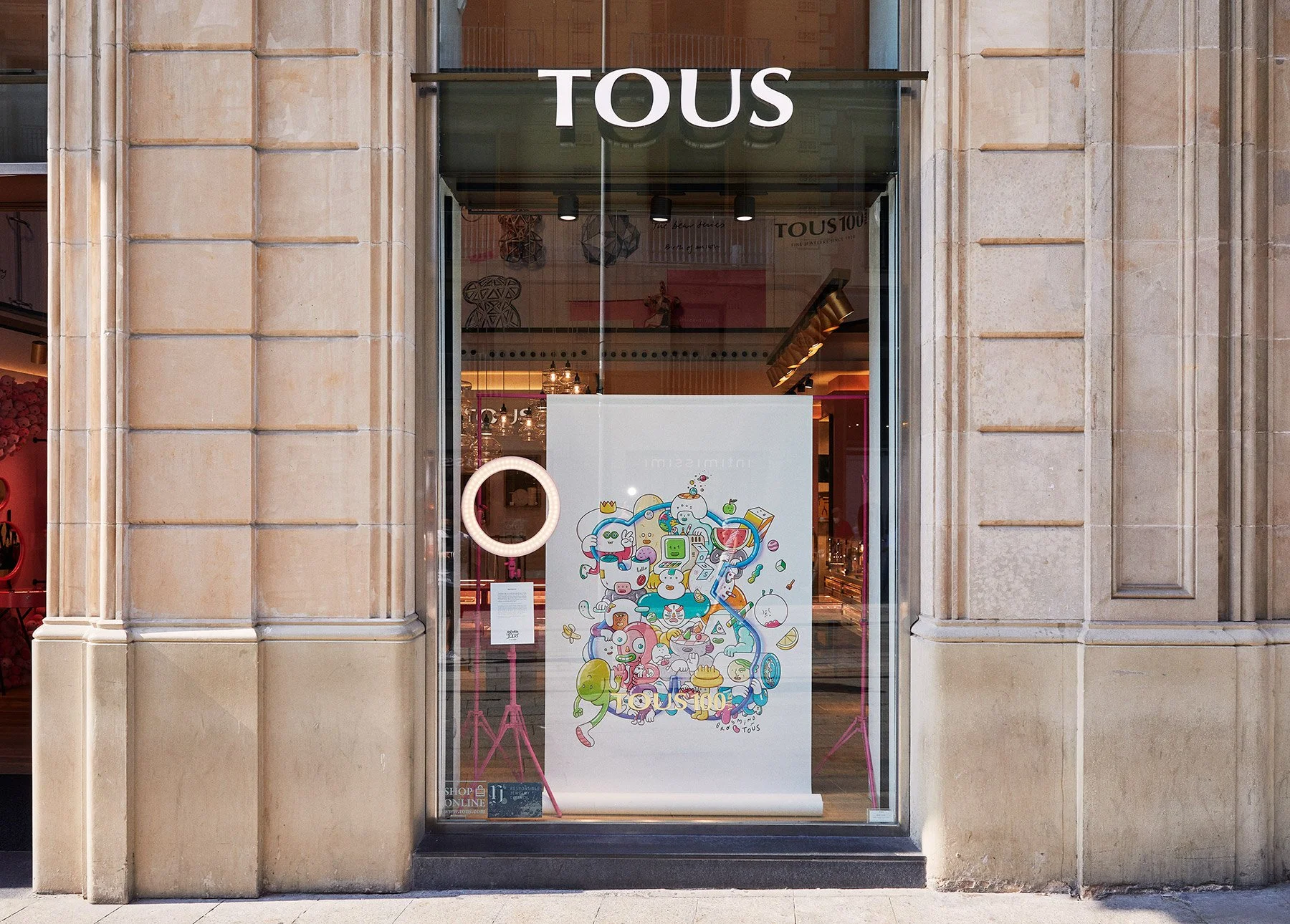 Outdoor storefront photo of a TOUS jewelry shop displaying the collaboration artwork poster. 