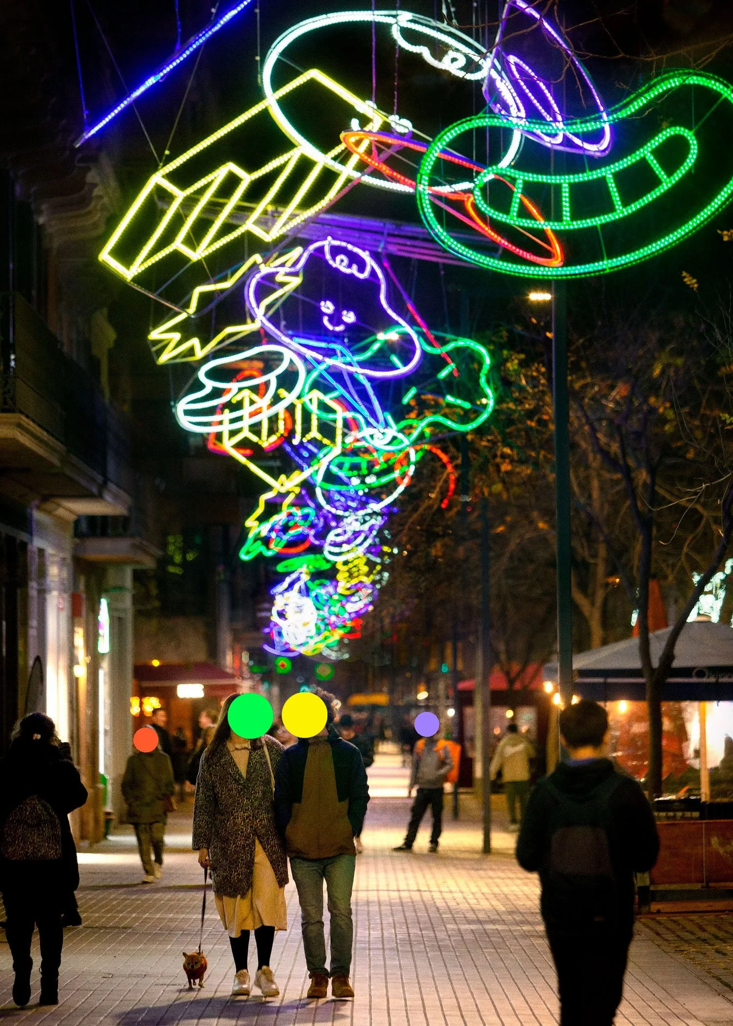 Couple walking down the Passeig de Sant Joan sidewalk beneath glowing, colorful Brosmind Christmas lights.