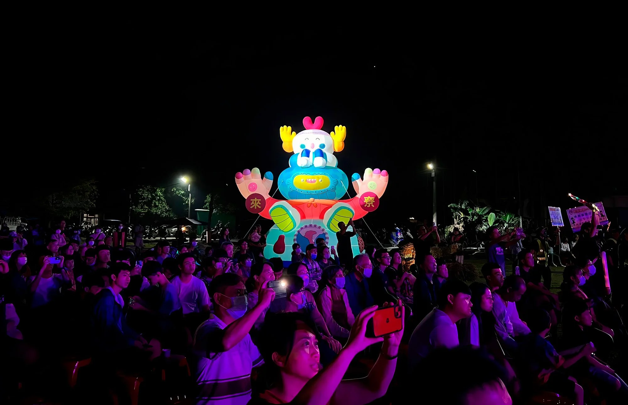 Giant illuminated totemic inflatable figure by Brosmind shining above a crowded night festival in Taiwan.
