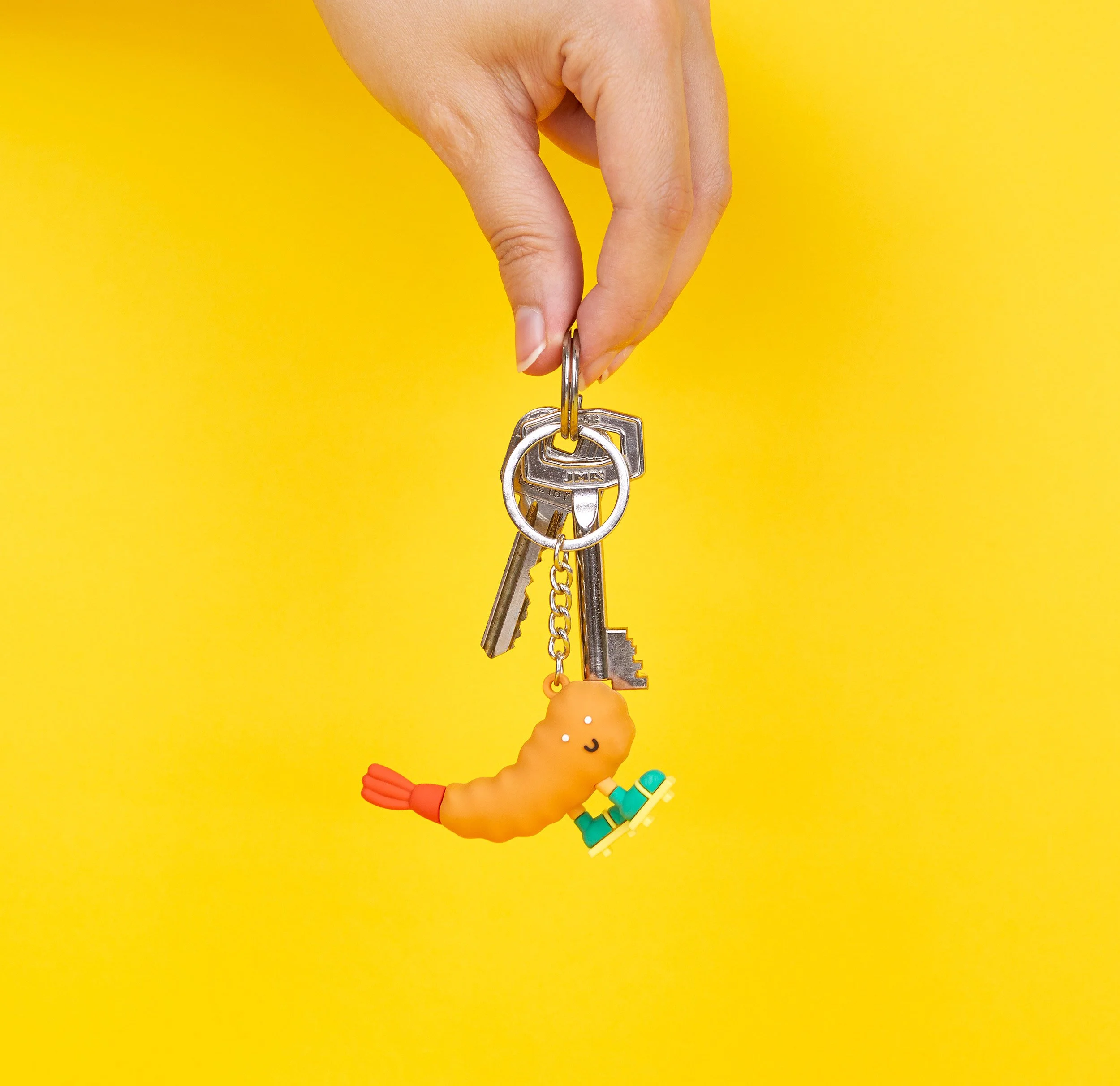 Hand holding the cute shrimp EBi-T ramen keychain with attached keys against a yellow background.