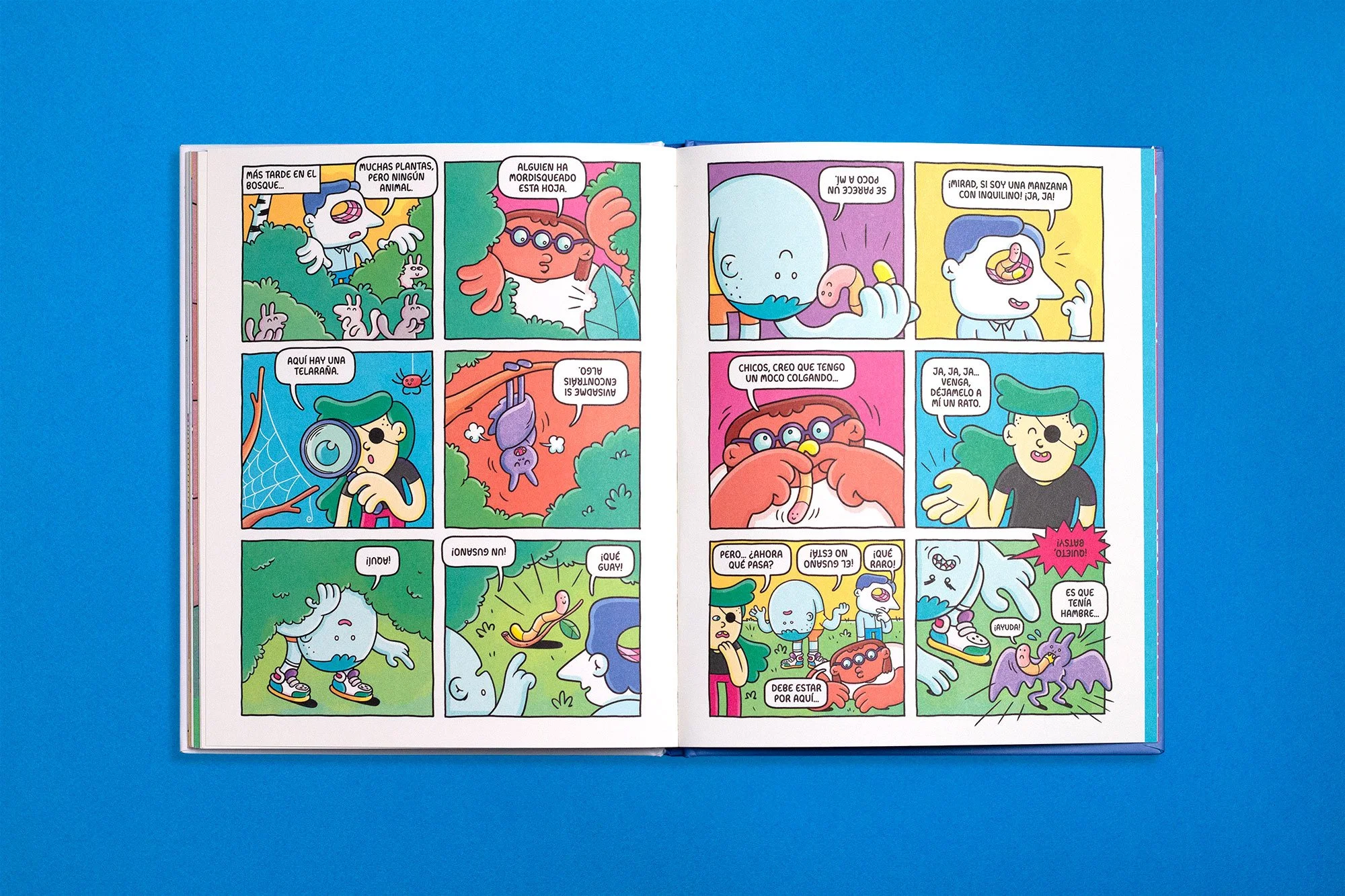 Flat lay photo of an open illustrated children's book featuring a colorful comic page with characters exploring a forest with wild animals.