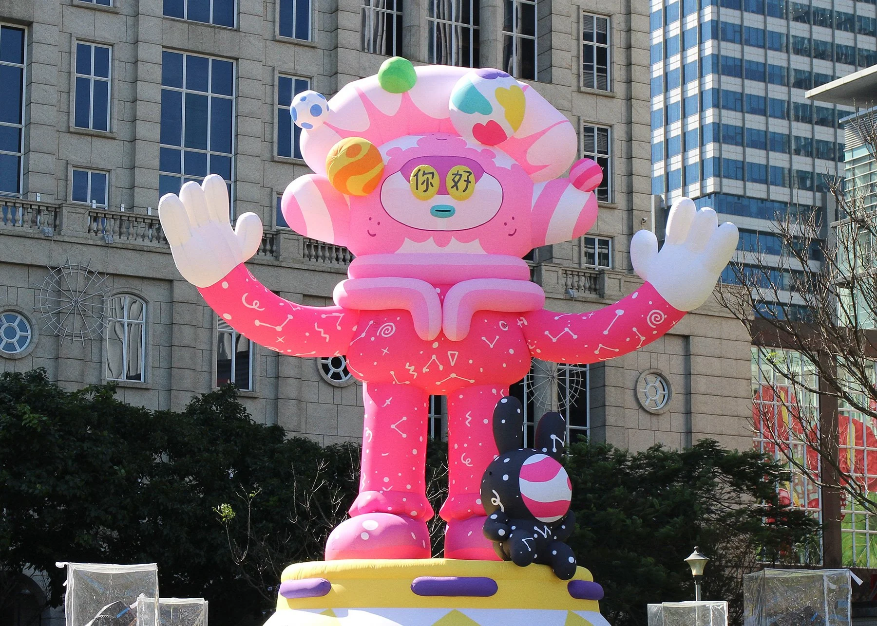 Vibrant pink 6-meter inflatable character with open arms in a city plaza daytime shot by Brosmind.