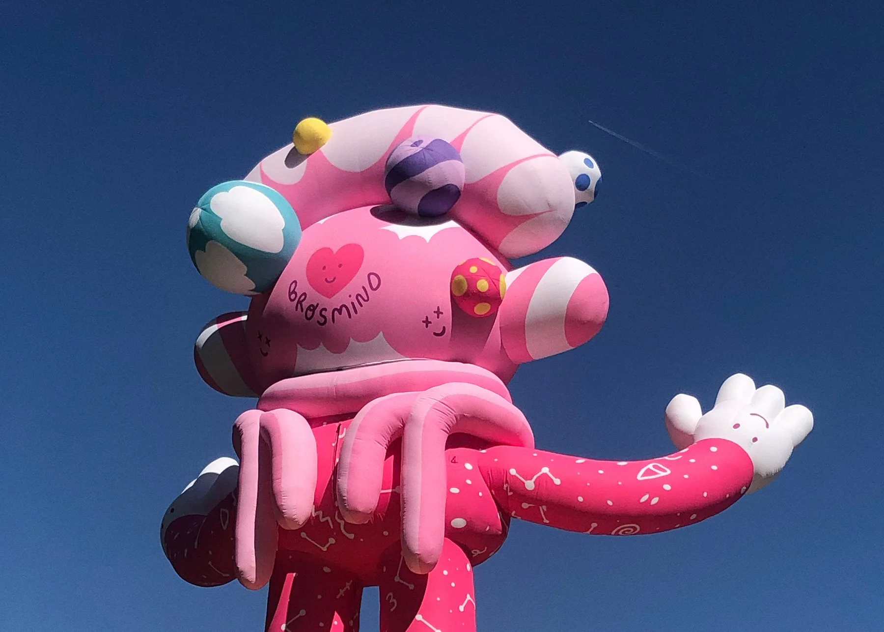 Daytime rear shot of the pink inflatable figure showing the Brosmind signature on its head against the sky.