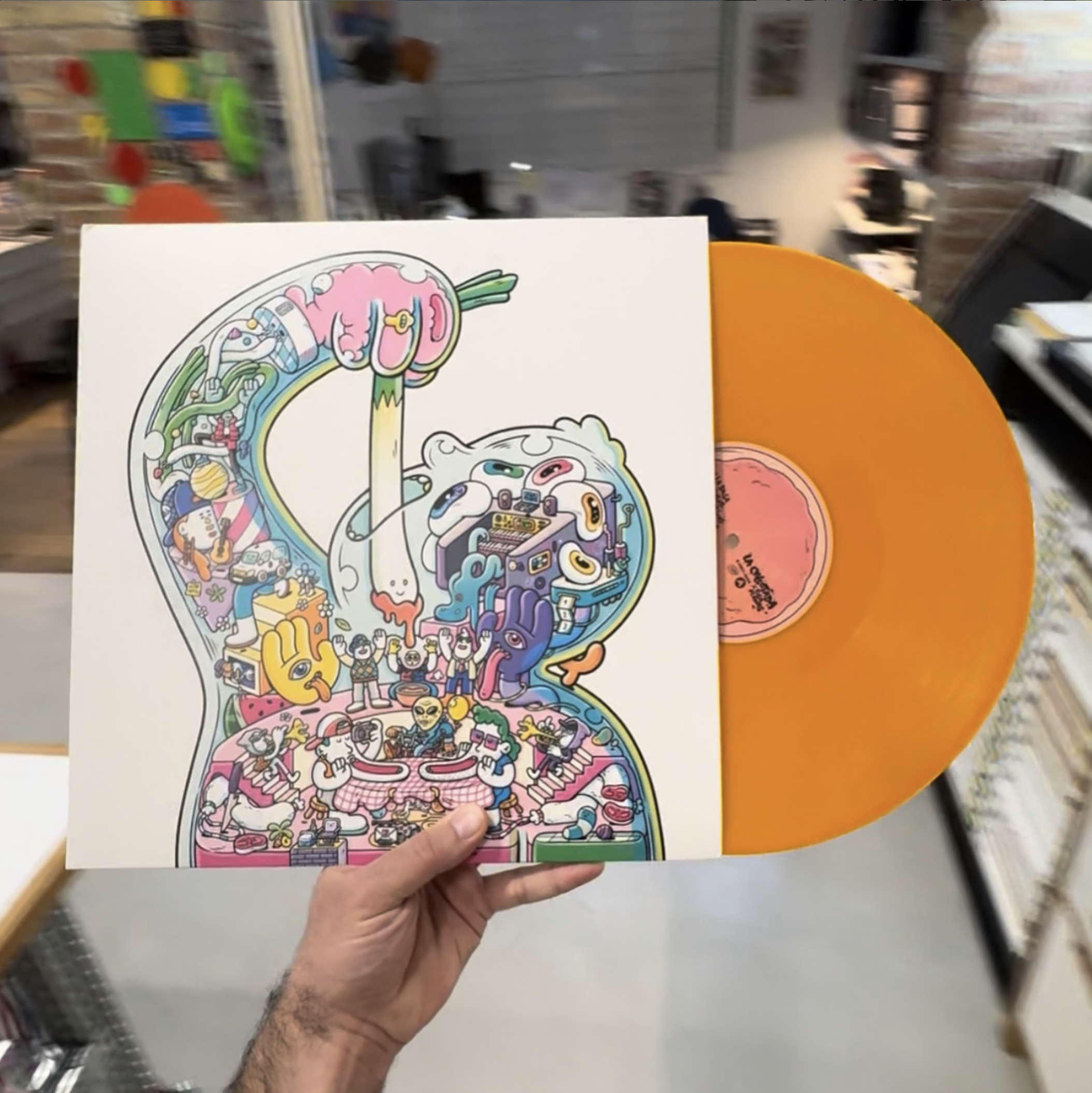 Close-up product photograph of a hand holding the physical vinyl album sleeve featuring Brosmind's custom cover illustration for Figa Flawas.