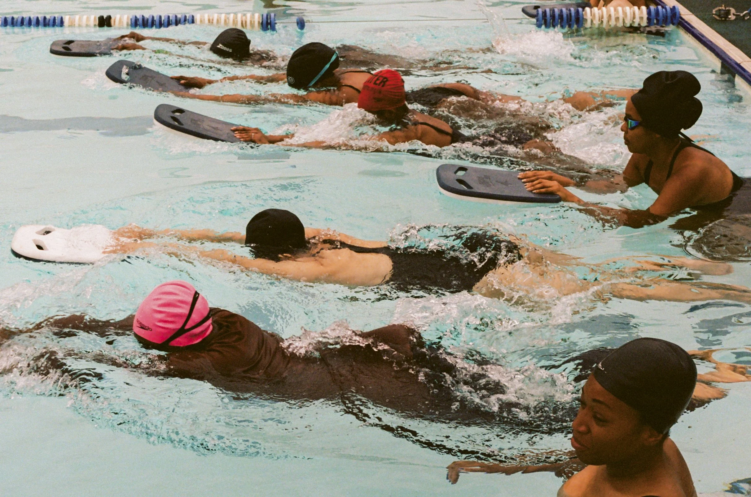 Swimmers practicing in an indoor swimming pool, wearing swim caps, goggles, and swimwear.