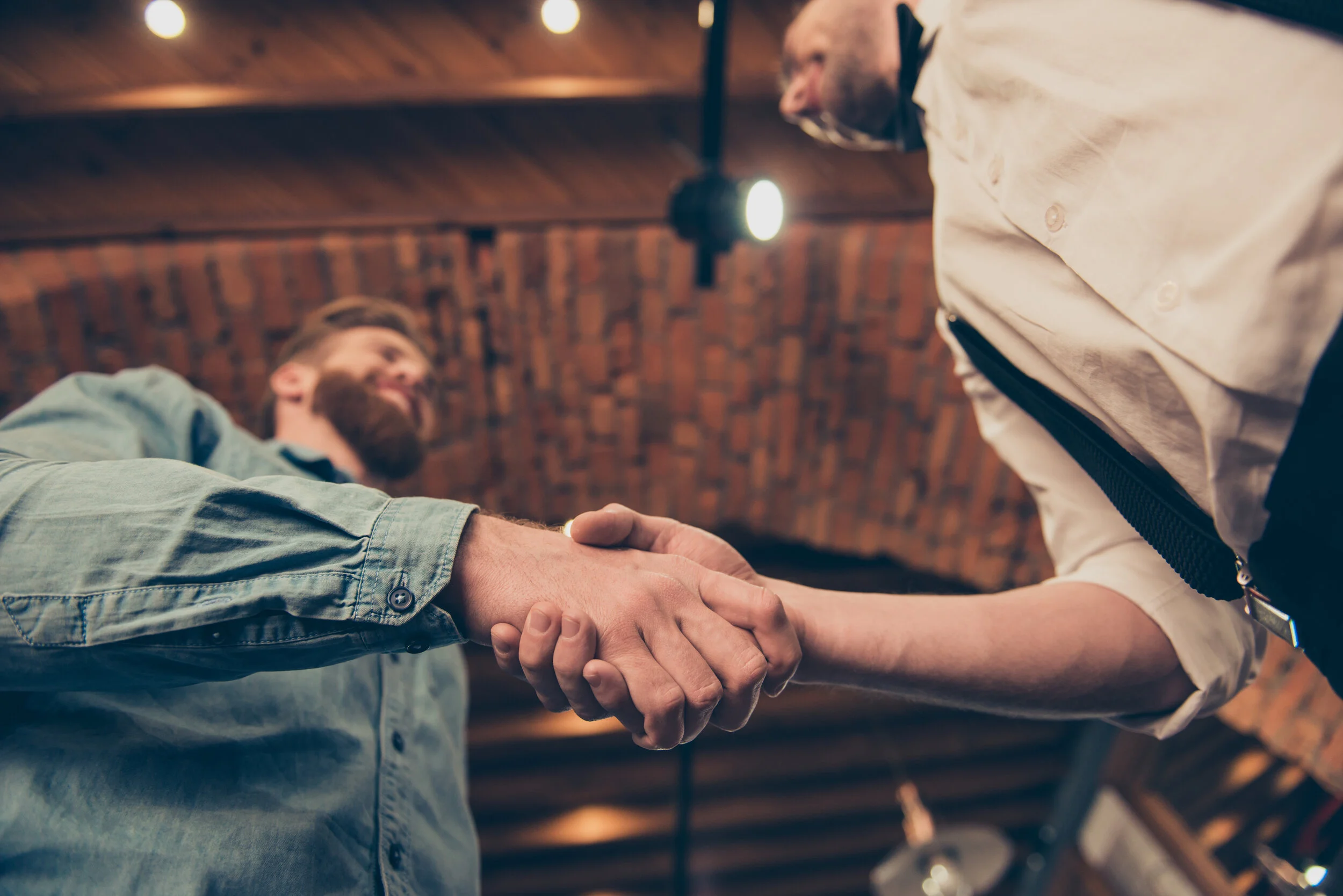 Low-angle-view-of-a-hanshake-of-the-red-bearded-client-and-classy-dressed-stylist-of-a-barber-shop-in-a-loft-style-939974002_7360x4912.jpeg