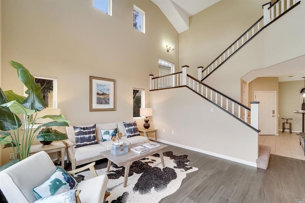 Staircase with banister stained a dark brown. Living room styled with modern furnishings, cow hide area rug, and big tropical plant