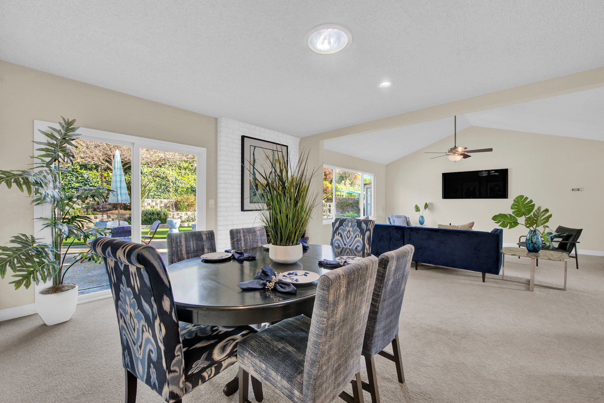 After of Home styling Living room dining room area. Clean open concept, high backed dining room chairs and dark oblong table. Lots of tropical plants for a pop of green around the room. Fresh ivory colored walls. A neutral color to sell a home fa