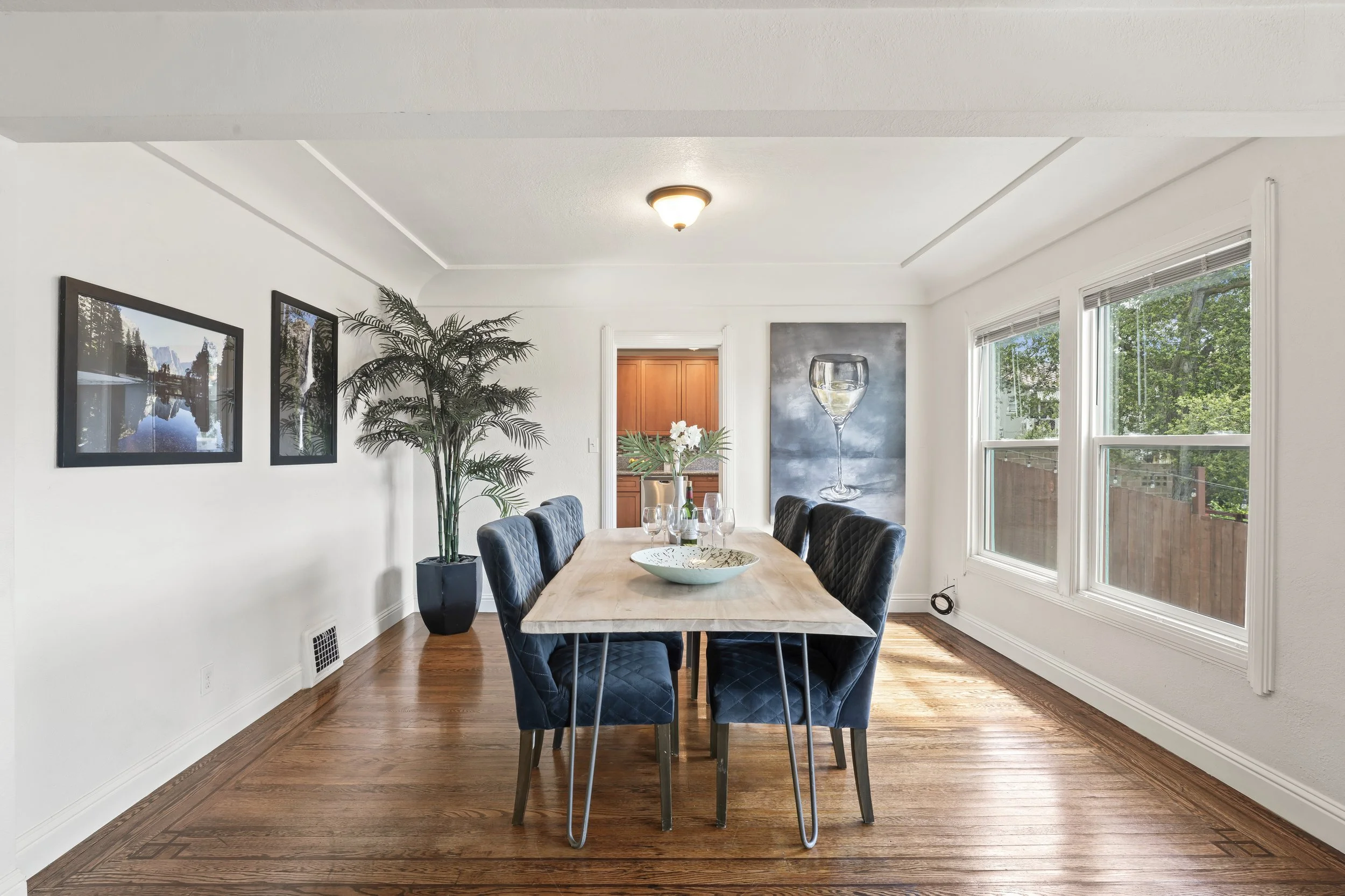 Dining room after Style it Staging professional staging services.  Modern fabric blue chairs, wood table top with metal legs.  Large art work and oversized tropical plant