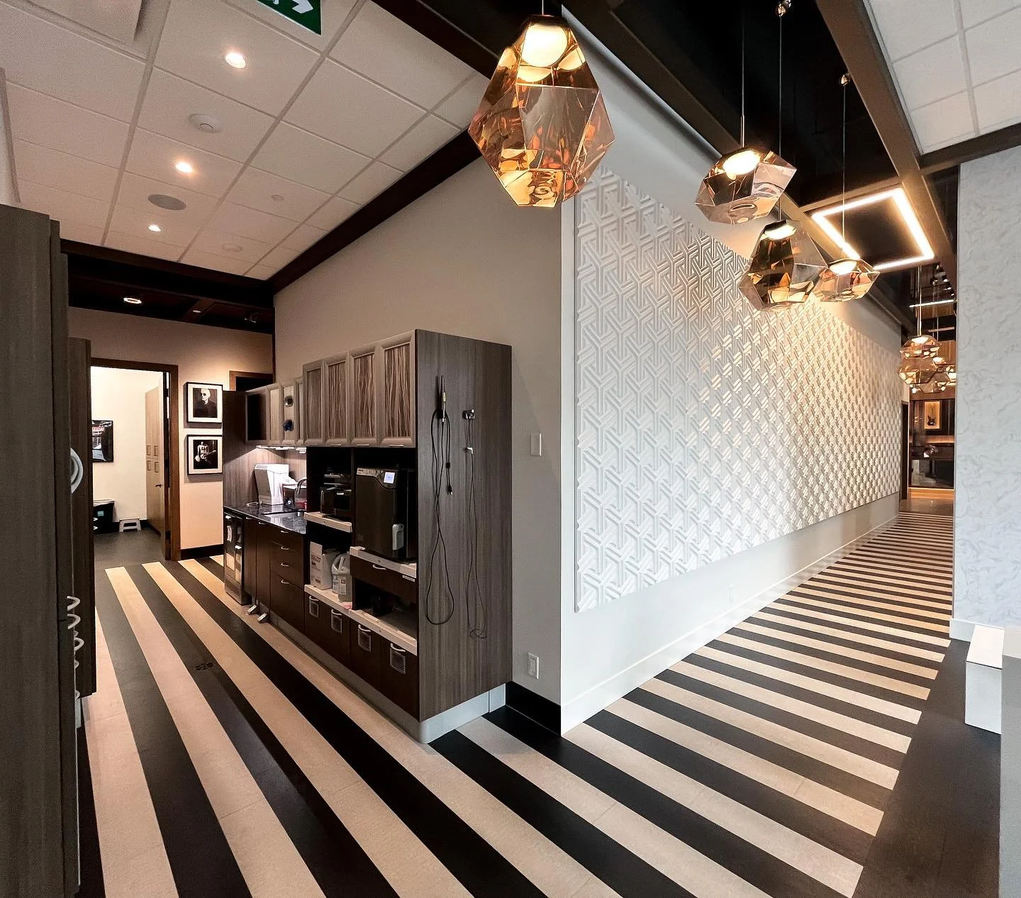 A modern hotel hallway featuring geometric patterned 3D wall panels, copper geometric pendant lights, and black and white striped flooring.