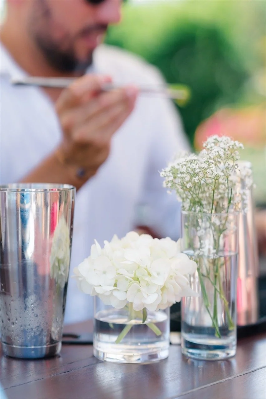 A person using chopsticks at an outdoor table with flowers in glass vases and a metal cocktail shaker.