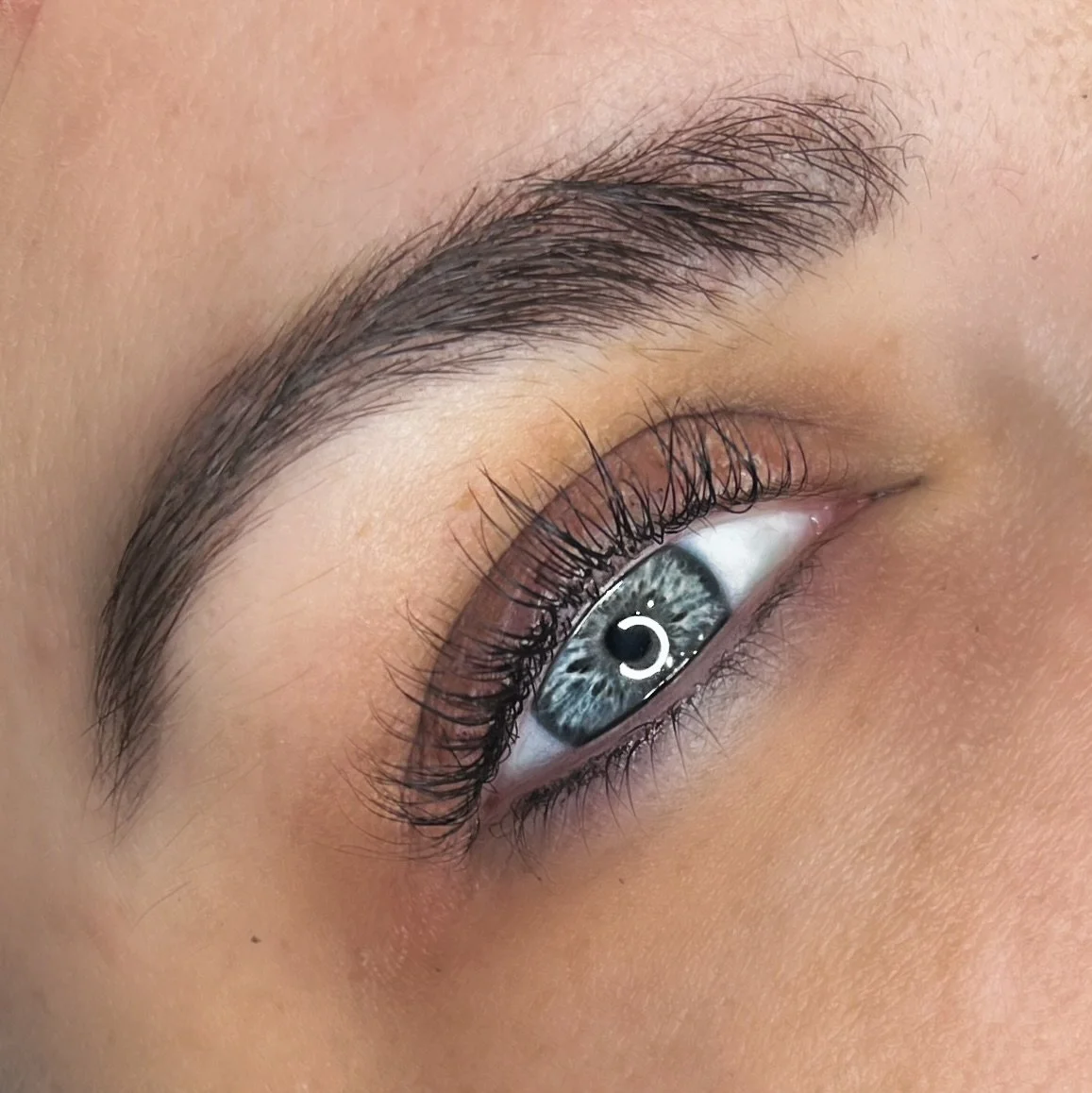 Close-up of a human eye with blue iris and long eyelashes, showing detailed eyebrow hairs and skin texture.