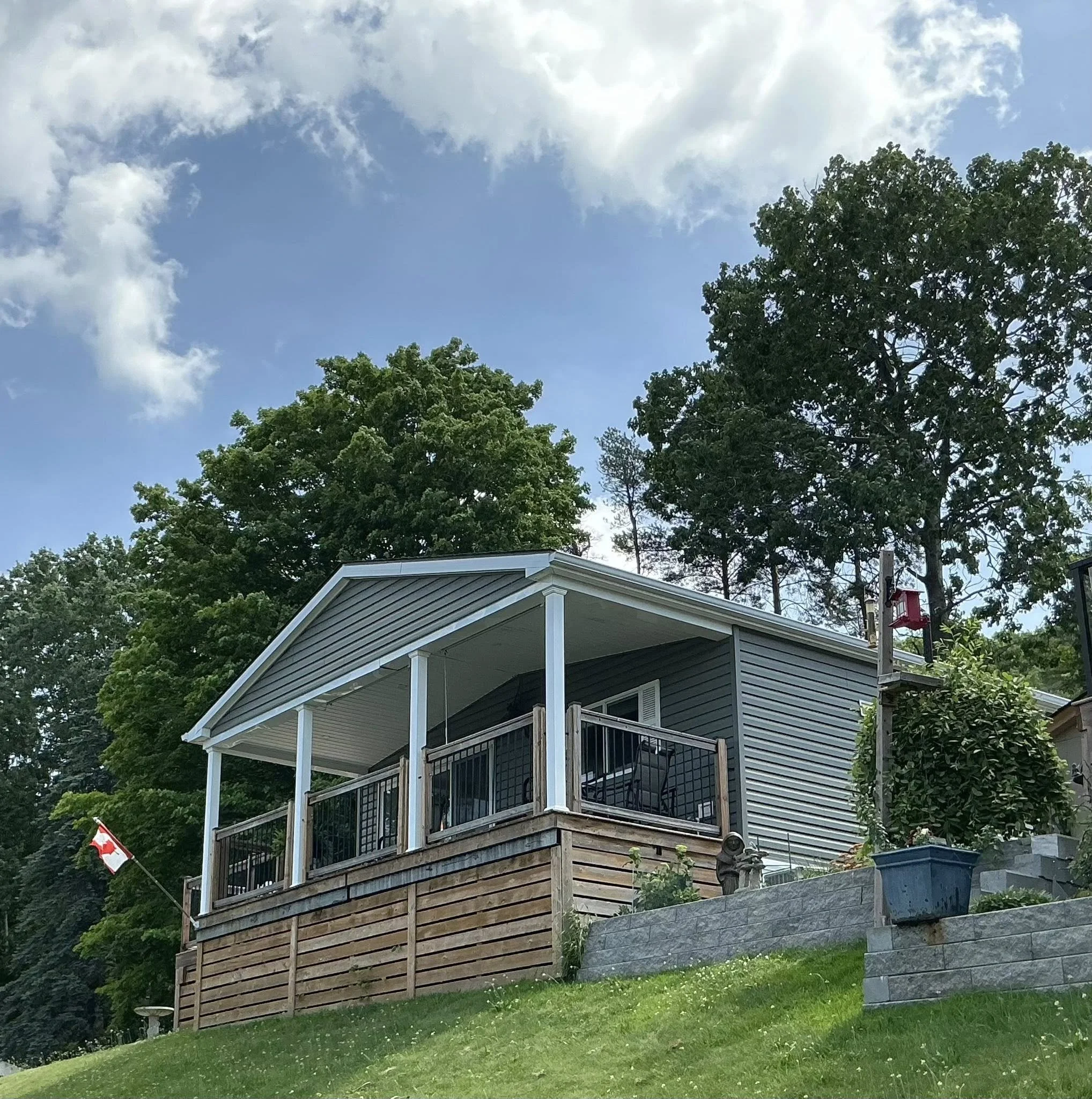 A house on a hill with a covered porch, trees in the background, and a Canadian flag to the left.
