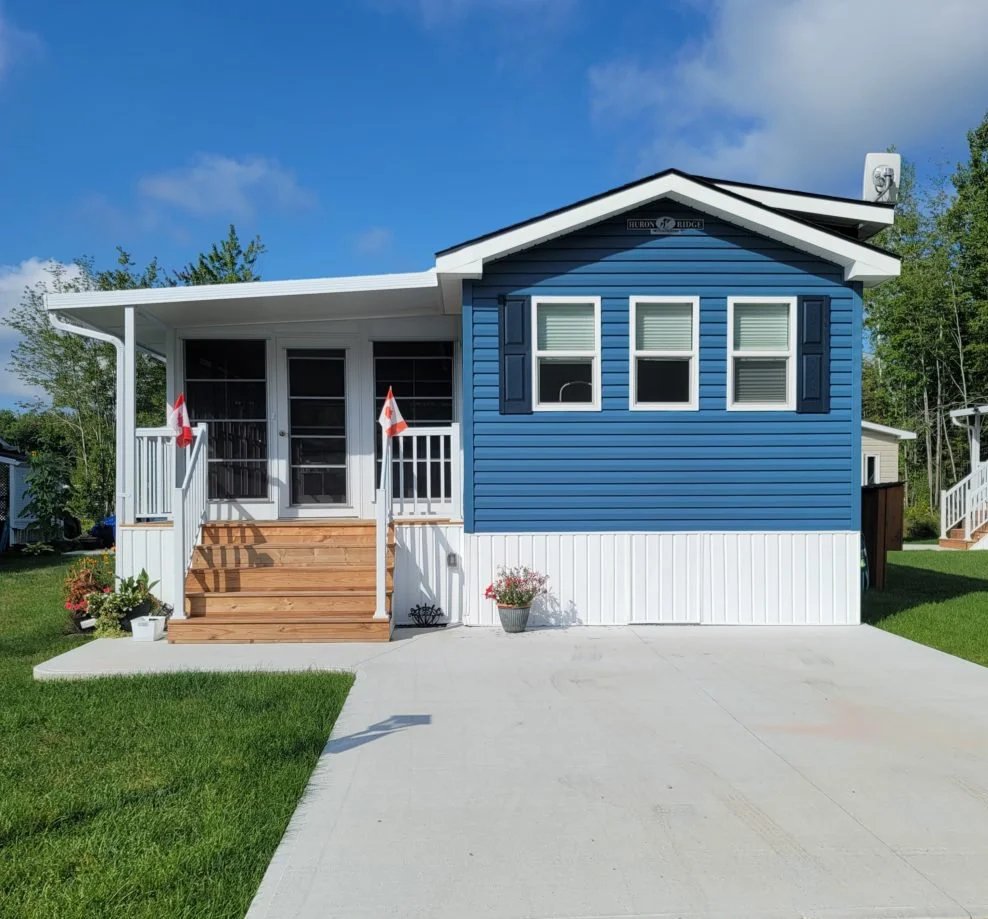 Small blue house with white trim, wooden steps, and a concrete driveway, set in a grassy yard.