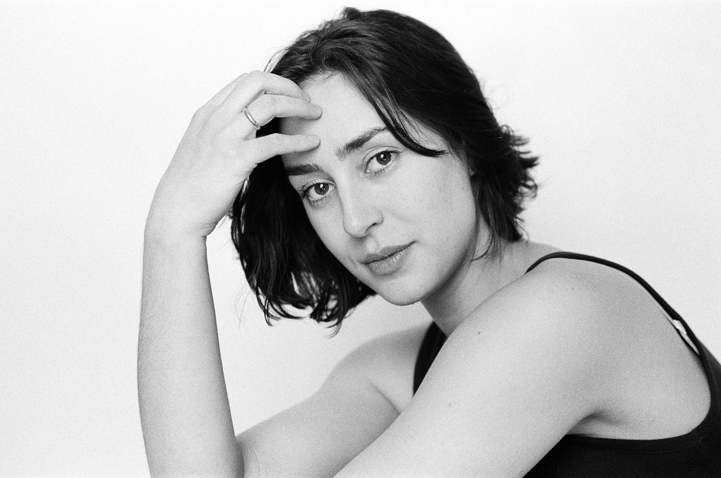 Black-and-white portrait of a woman with short, wavy hair, looking at the camera with her head resting on her hand.