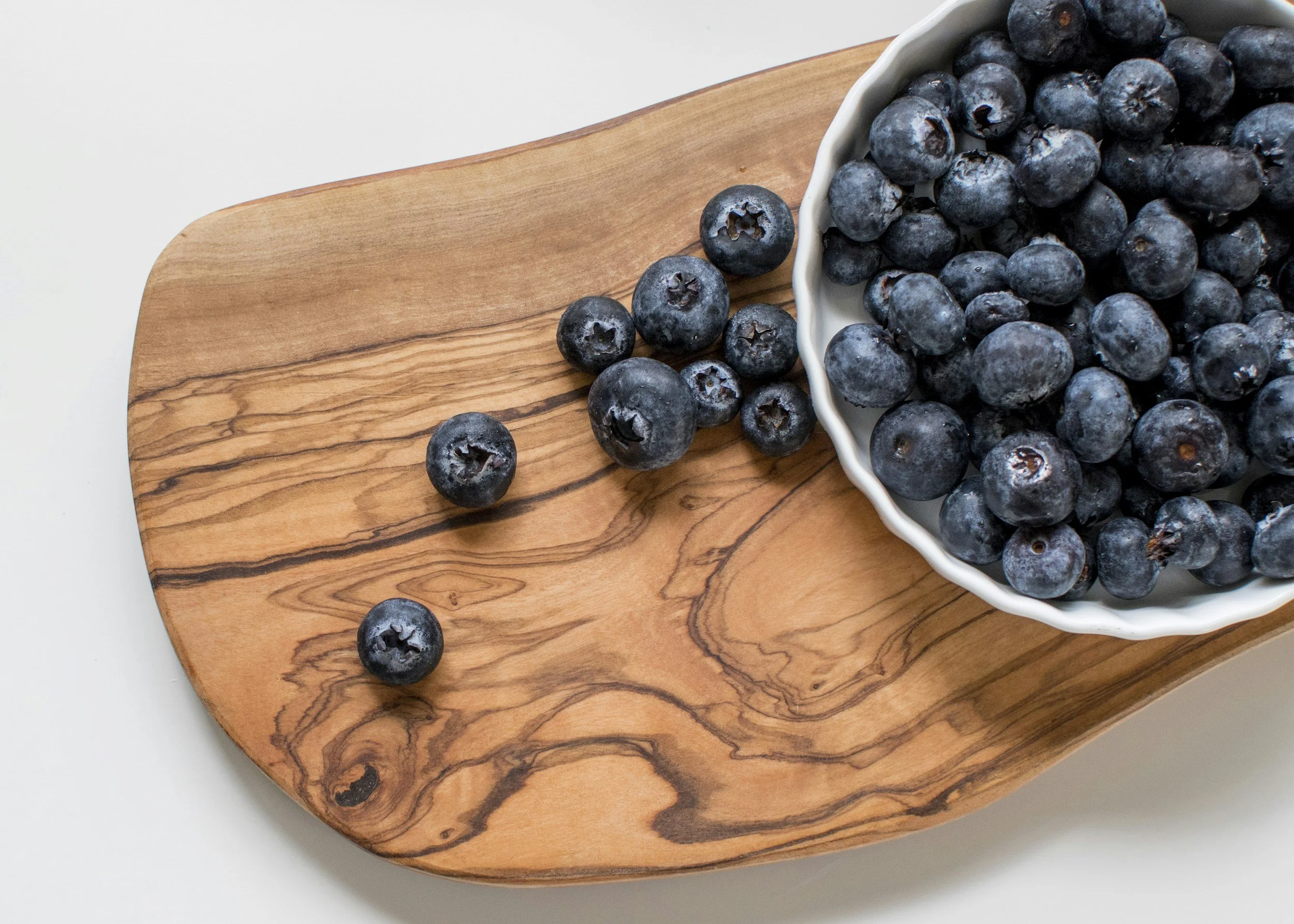 Fresh blueberries in a white bowl on a wooden surface with a plain background.