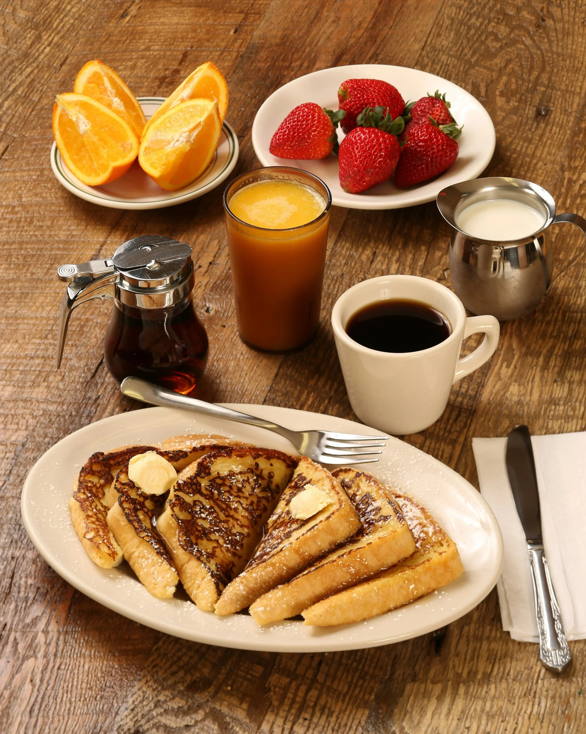 Plate of French toast topped with butter, powdered sugar, and syrup, with fresh strawberries and orange slices, on a rustic wooden table.