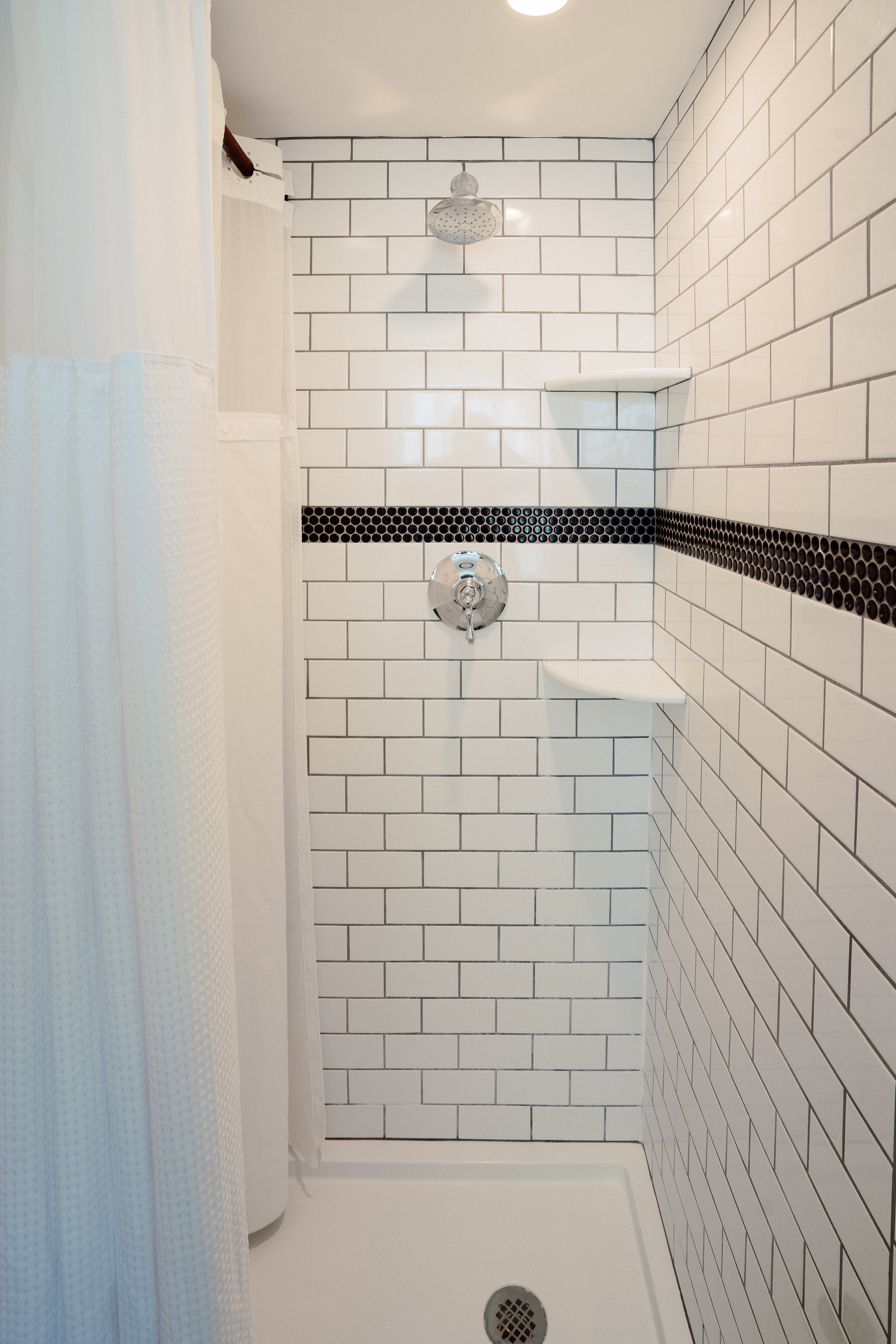 The Bathroom of the Bay Shore Room. Black and White Vintage Tiles, White Draw Curtain and Silver Hardware