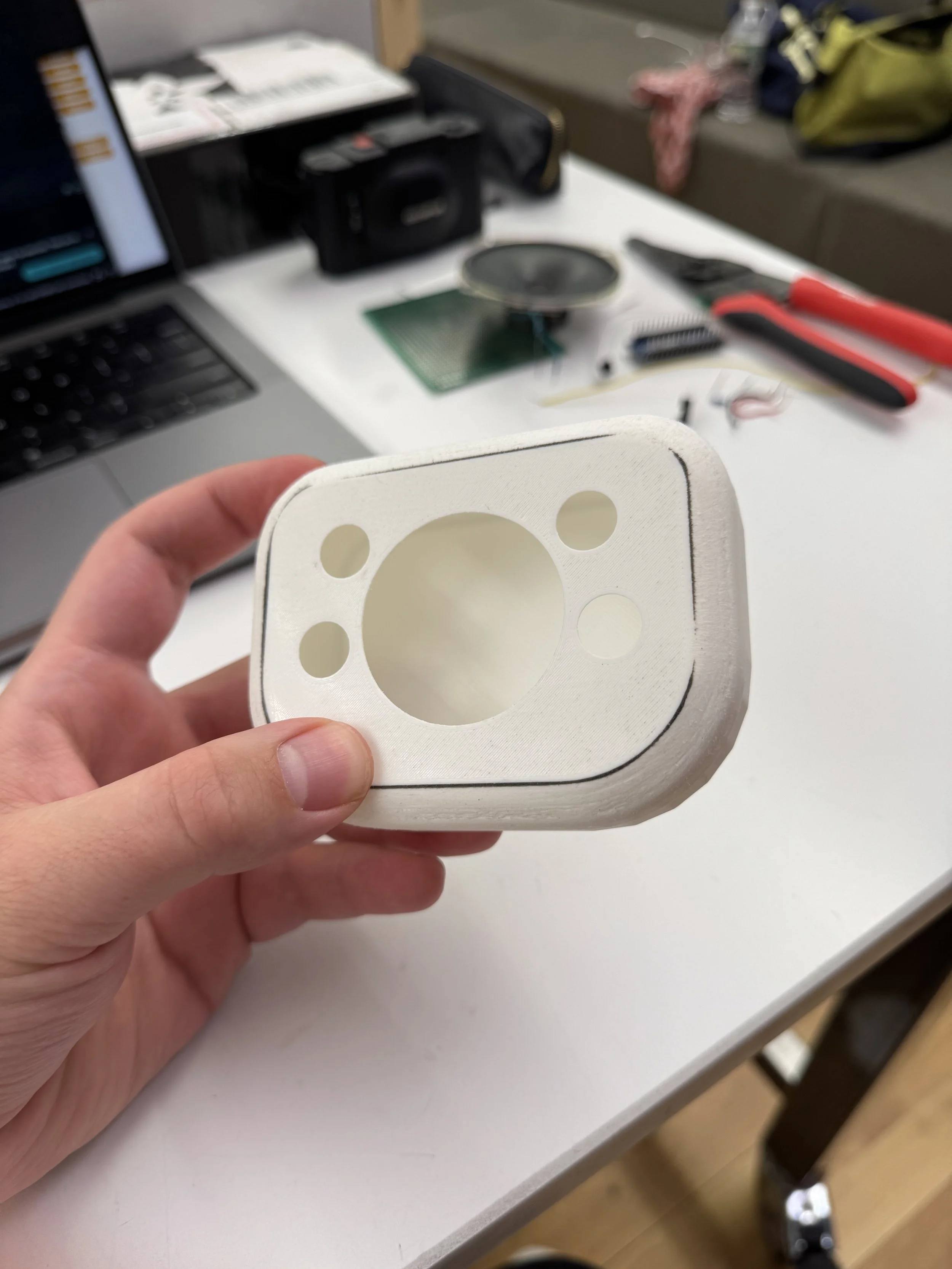 Person holding a 3D-printed white part with a large central hole and four smaller holes.