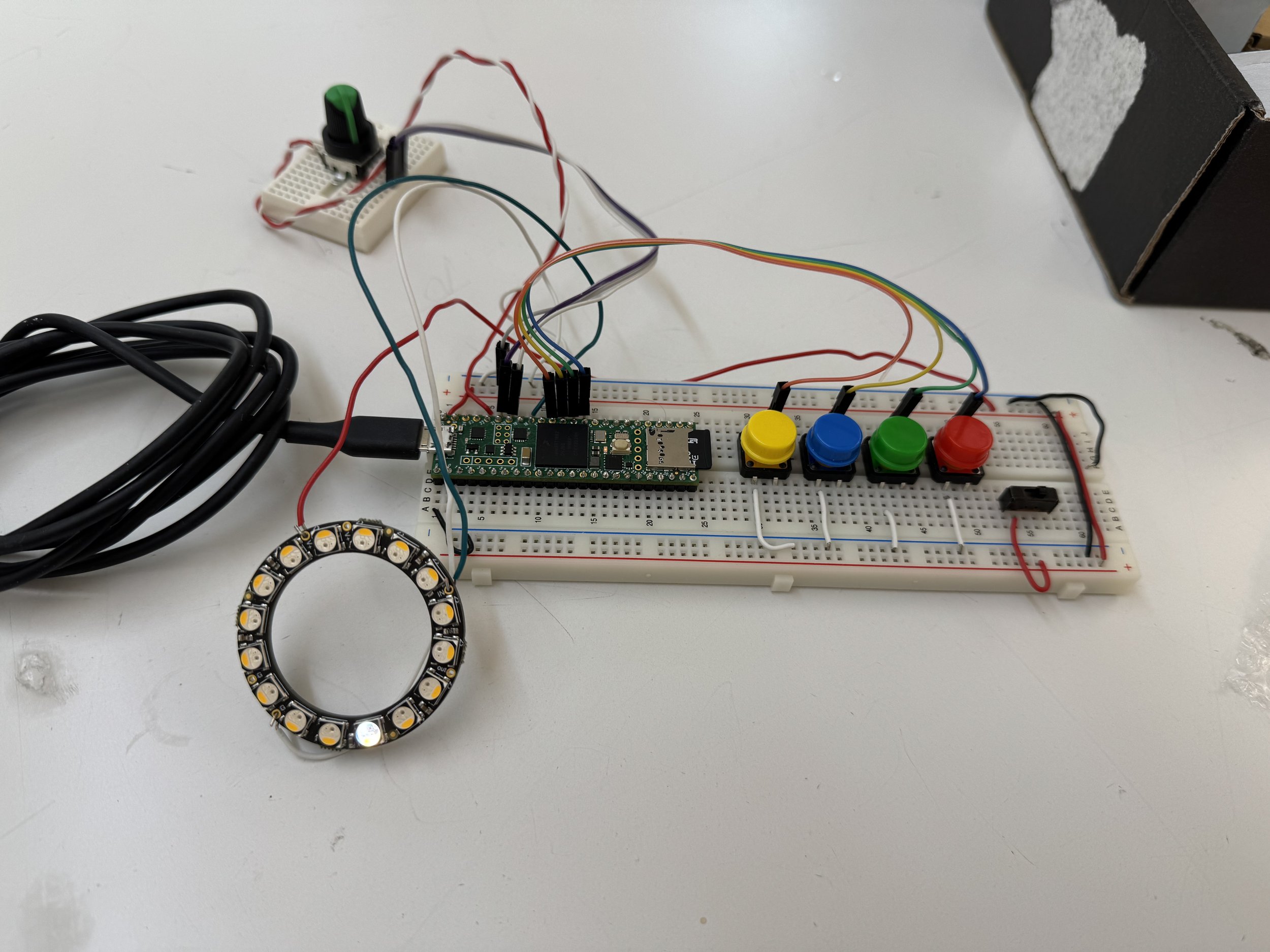 Electronic circuit on a breadboard with colorful buttons, wiring, and sensors, including a ring of LED lights.
