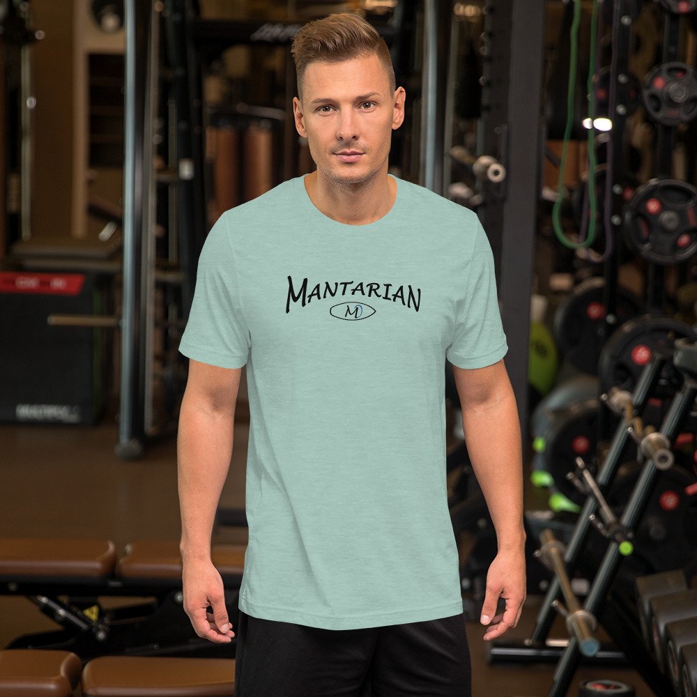 A man with short hair and light skin looking at the camera, standing in a gym with workout equipment behind him. He is wearing a light green T-shirt that has the word 'MANTARIAN' and a small oval with the letter 'M' printed on it.