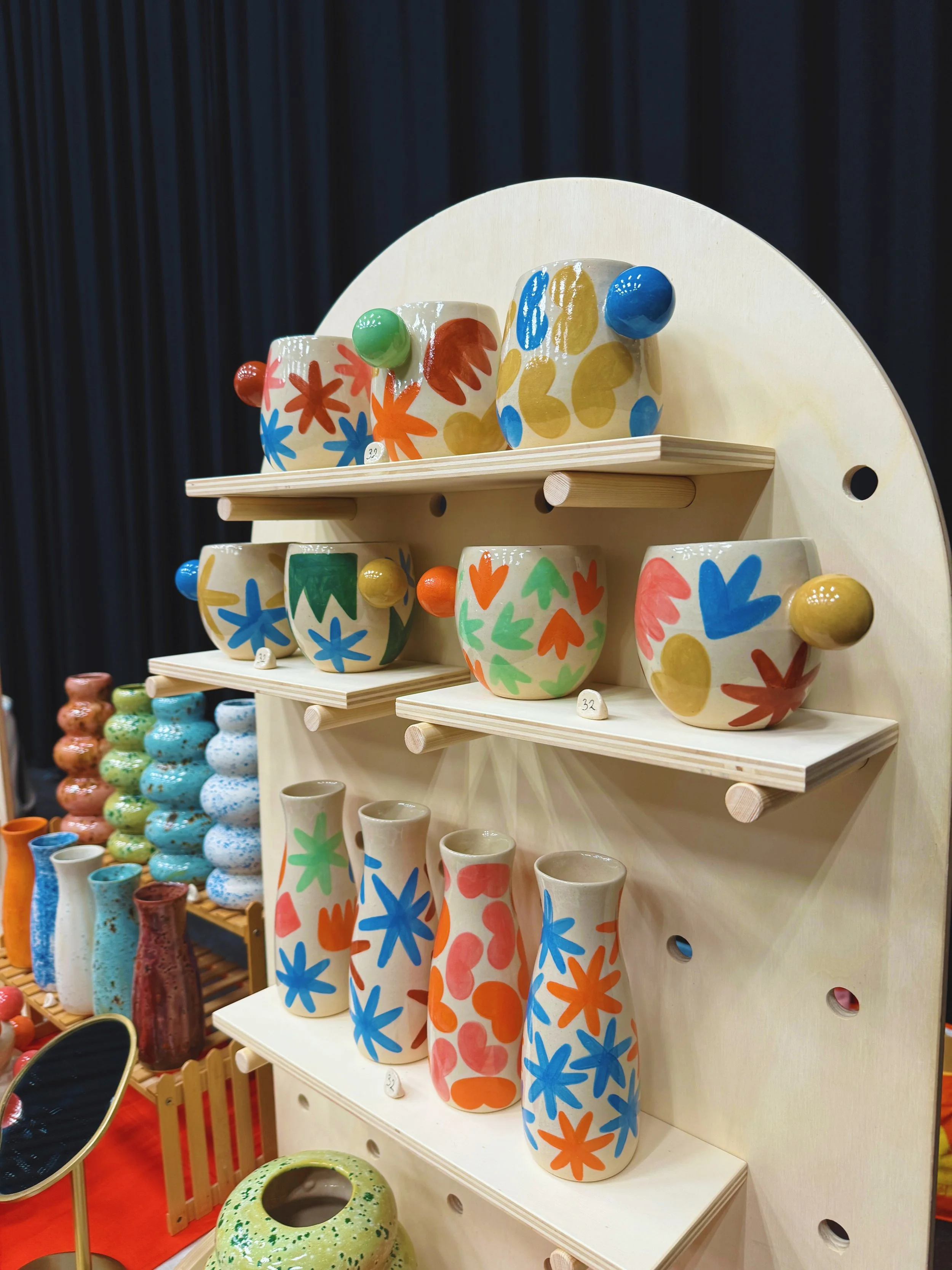 Colorful ceramic vases on a wooden display stand with dark curtains in the background.