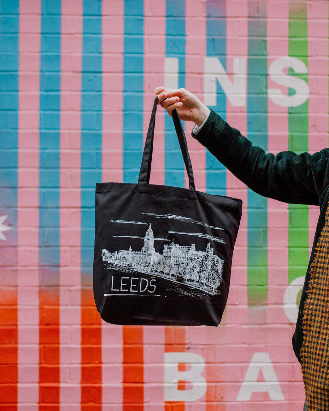 An LGBTQ+ illustration studio prints locally, using UK printers, 100% cotton tea towels, and organic tote bags. Monochrome skylines honour memory and place. Shoppers support sustainable production, inclusive small business, and meaningful art that sp